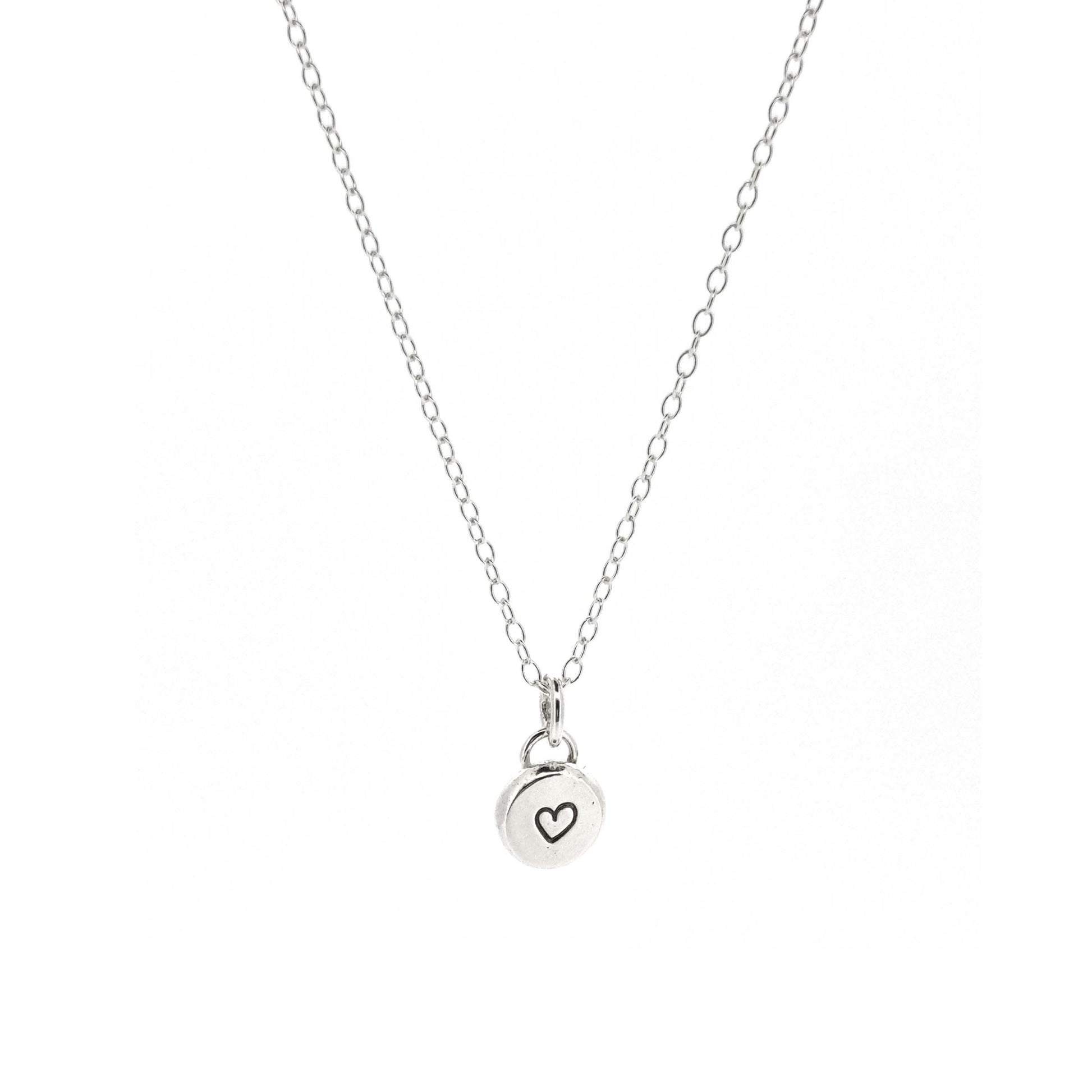 A round silver flat pebble pendant with a black heart in the centre. On a silver chain. Small.