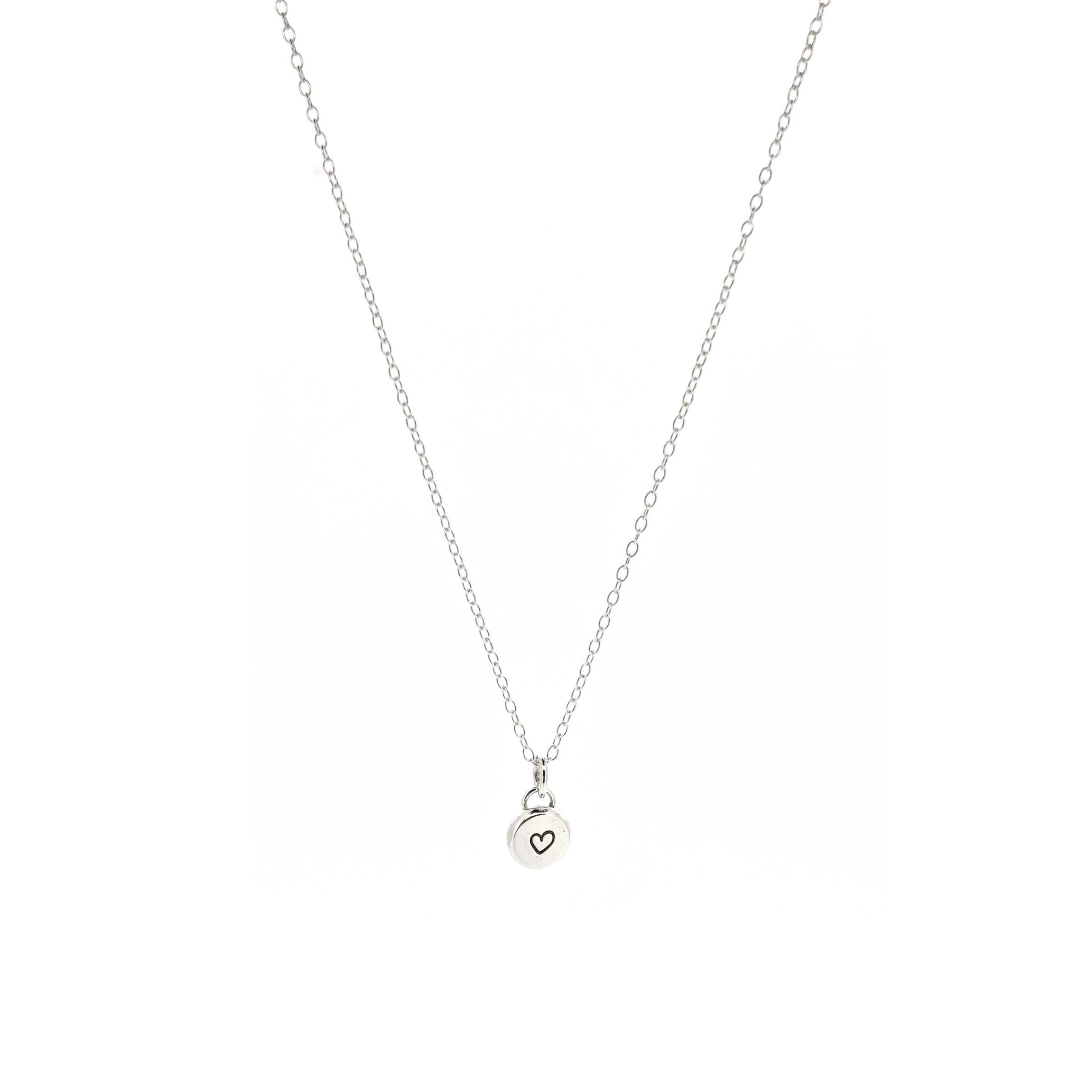 A round silver flat pebble pendant with a black heart in the centre. On a silver chain. Small.
