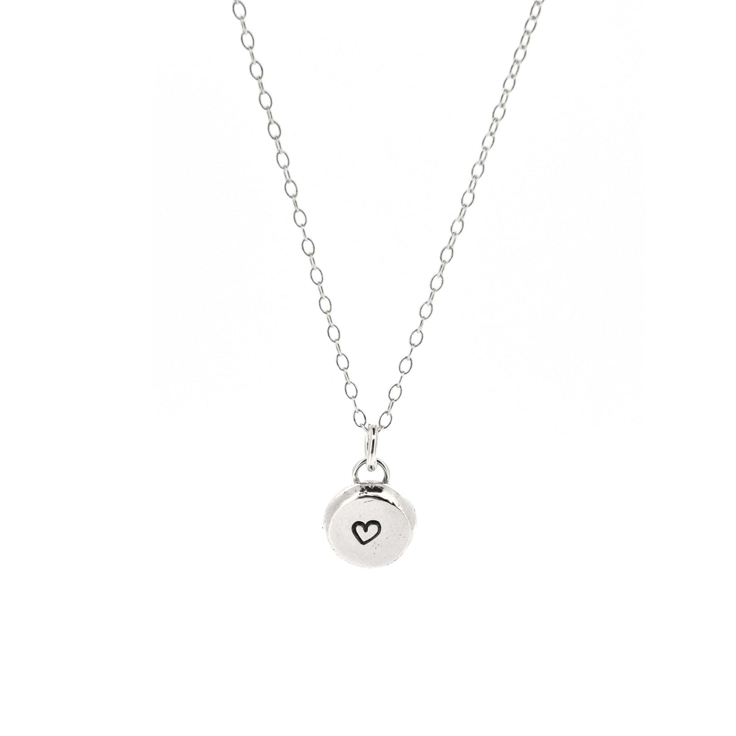 A round silver flat pebble pendant with a black heart in the centre. On a silver chain. Medium.
