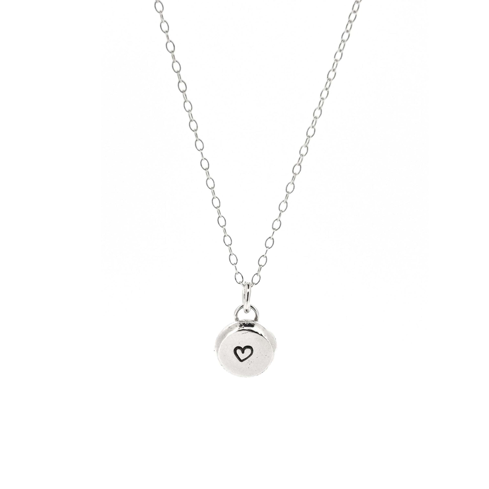 A round silver flat pebble pendant with a black heart in the centre. On a silver chain. Medium.