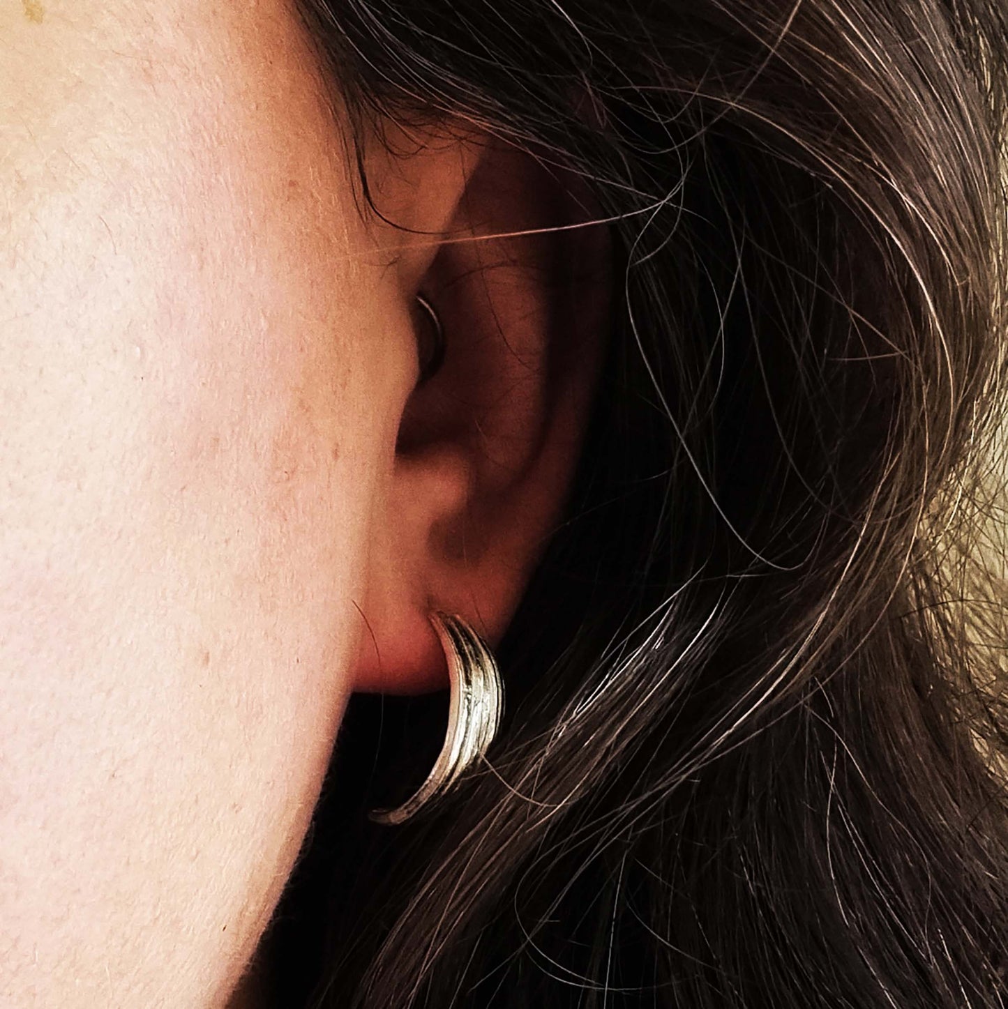 Silver line textured half hoop earrings. Pictured being worn.