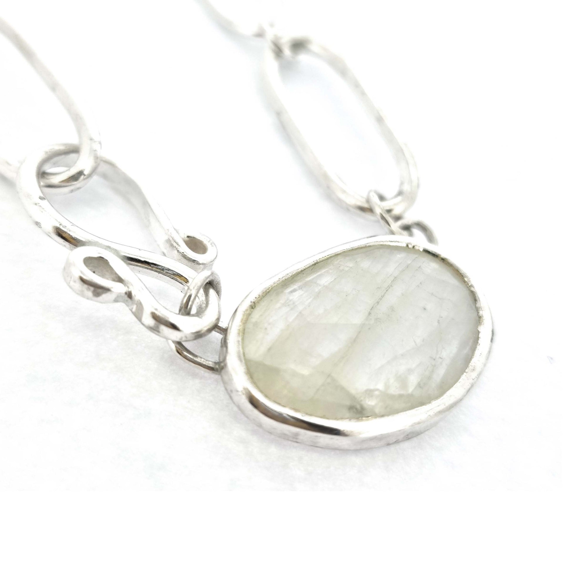 A silver chain necklace with open oblong links of different sizes, an s-clasp and a moonstone slice in a bezel setting.