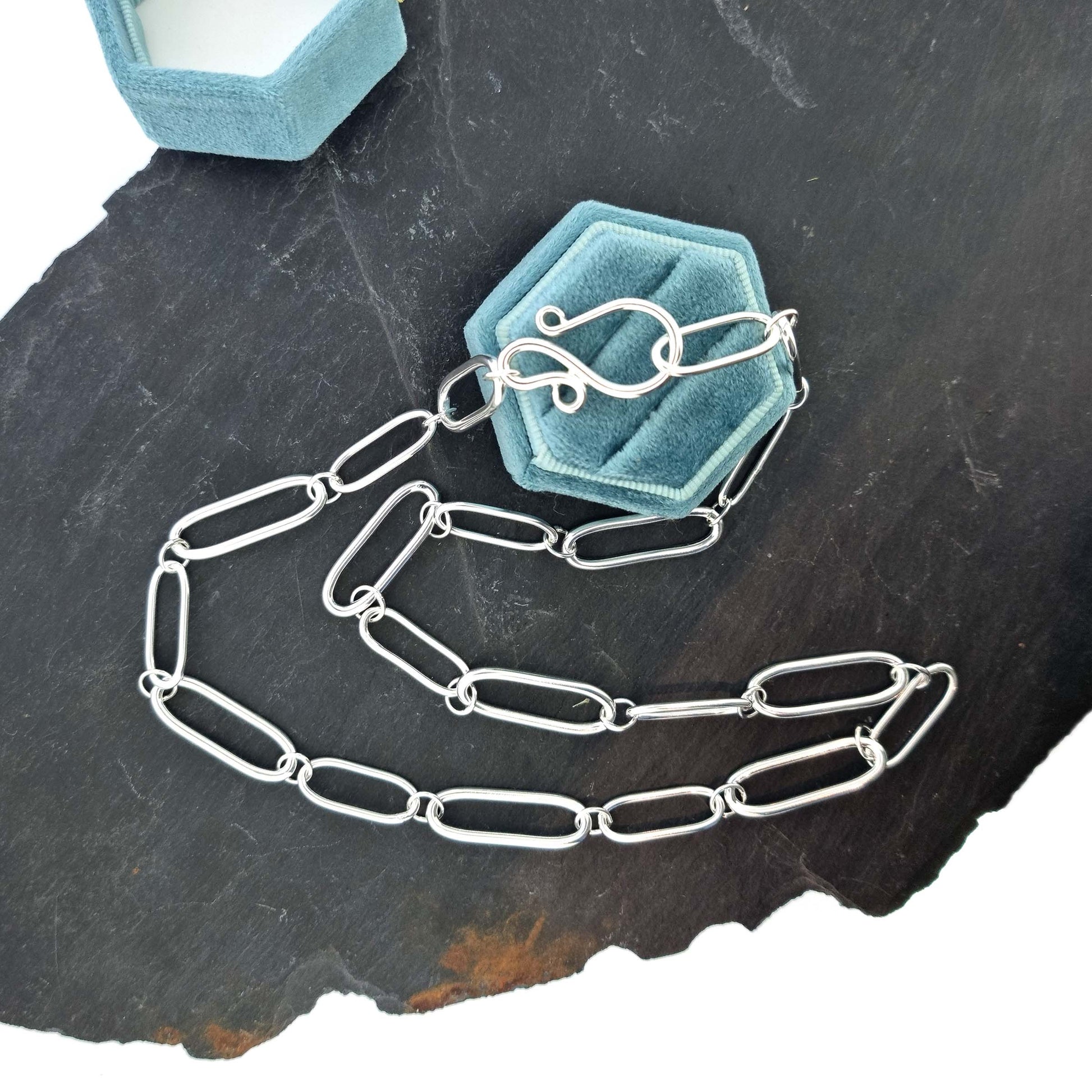 A silver chain necklace with open oblong links of different sizes. Pictured on a jewellery box.