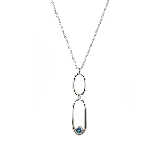 A silver pendant featuring 2 open oblong shaped of different sizes with a blue topaz gemstone set inside one curve. On a silver chain.