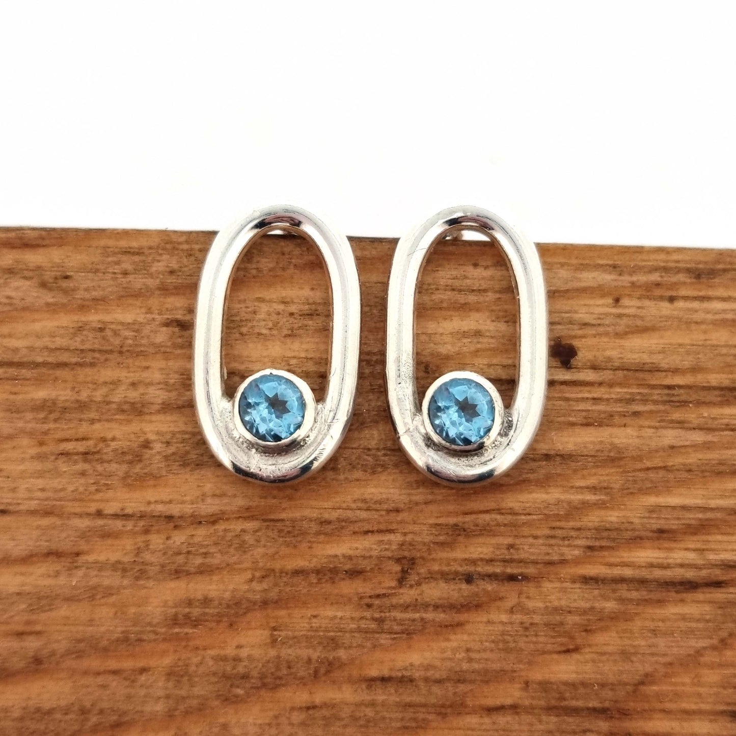 Silver open oblong stud earrings with a blue topaz gemstone set inside one curve.