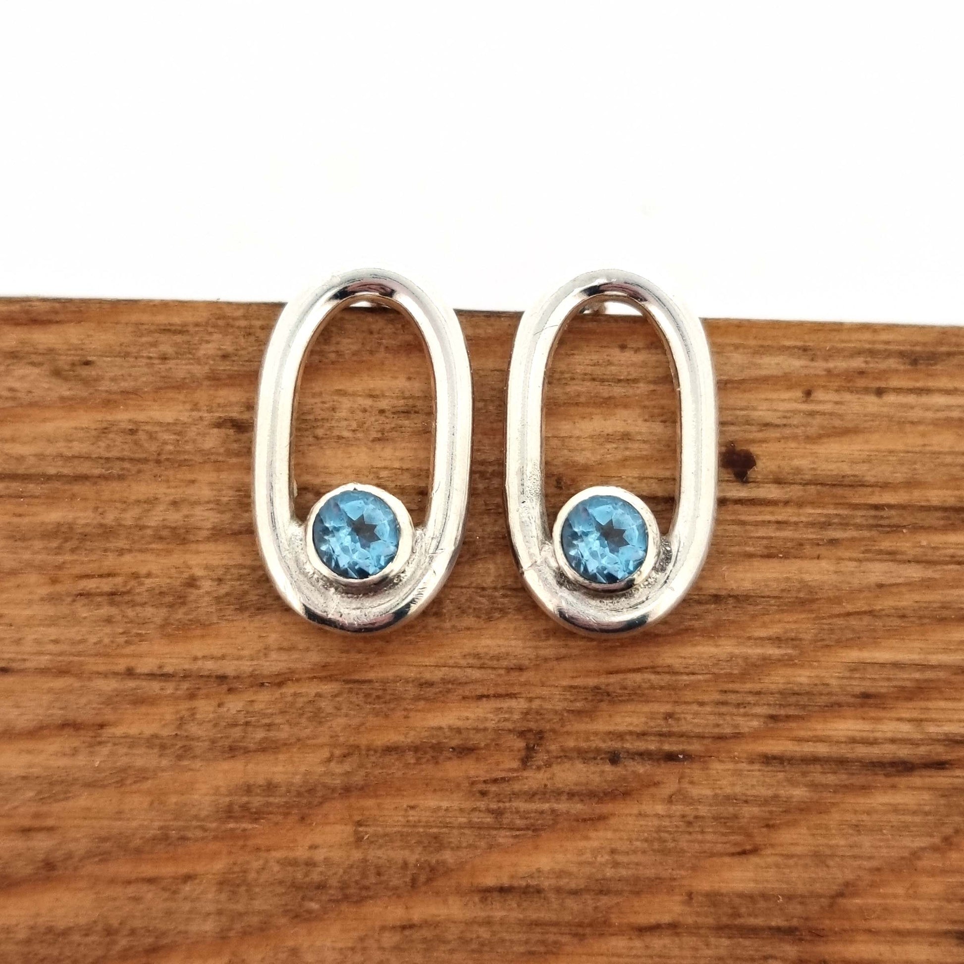 Silver open oblong stud earrings with a blue topaz gemstone set inside one curve.