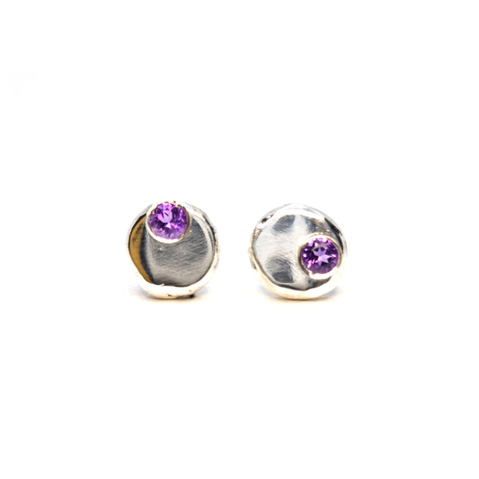 Silver round flat pebble stud earrings with round purple amethyst gemstones set off-centre.