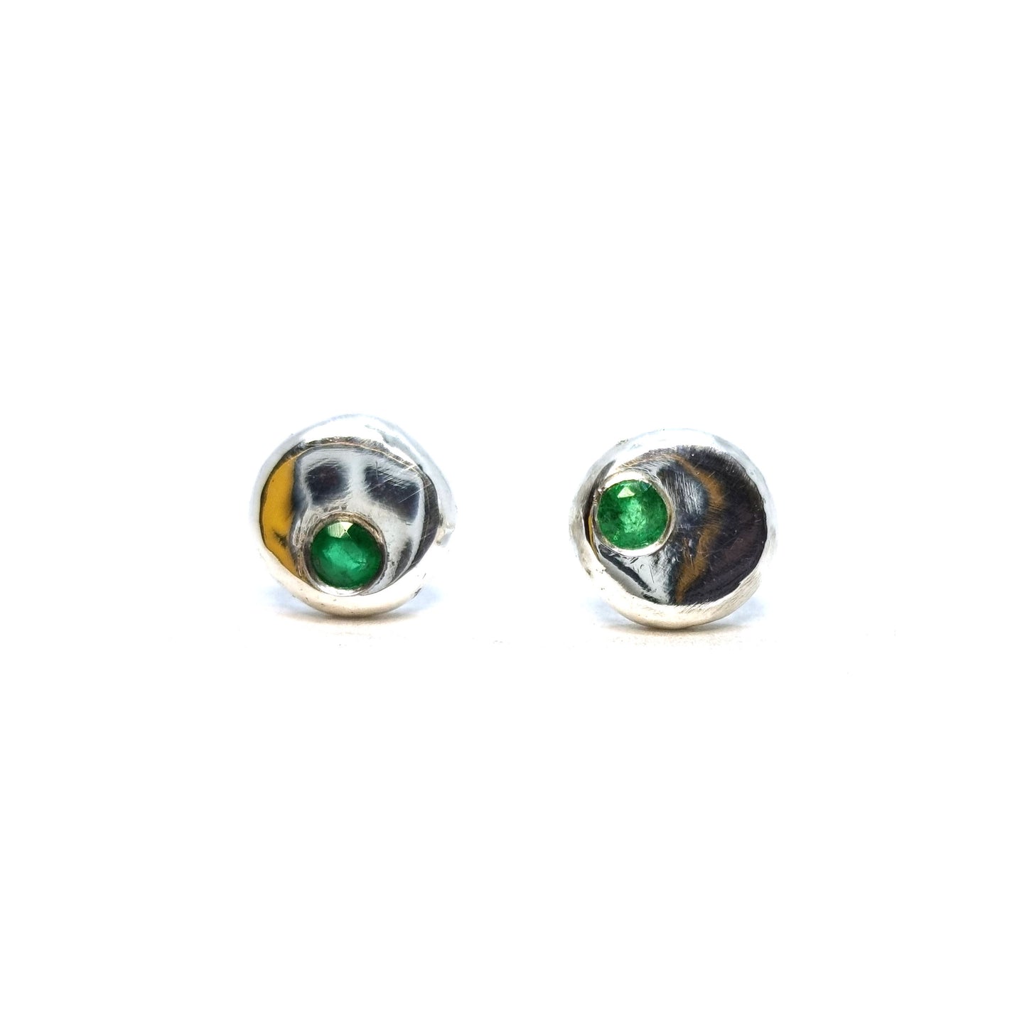 Round silver pebble stud earrings with green emerald gemstones set off-centre.