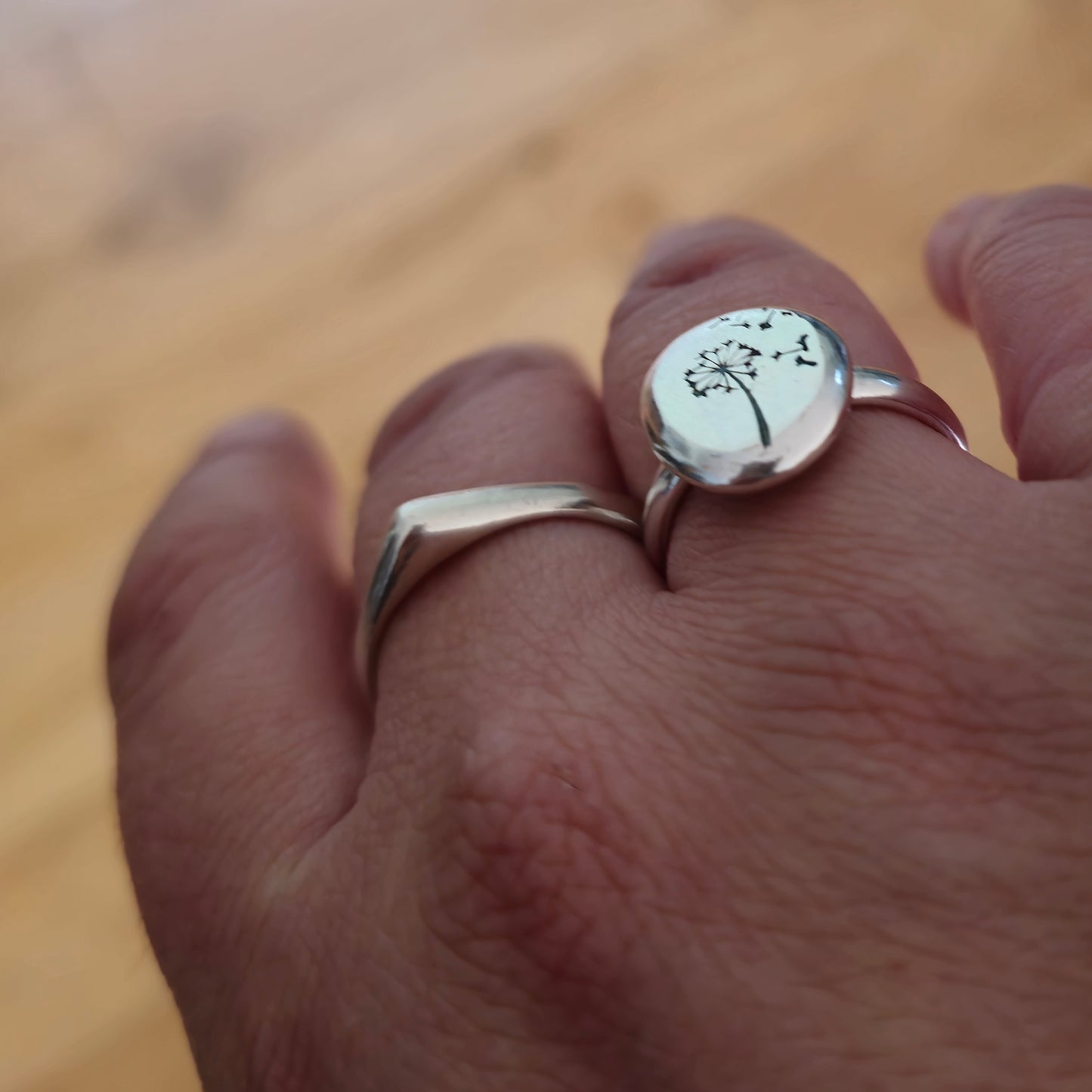 A silver ring which comes to a soft point at the top. Shown on a hand.