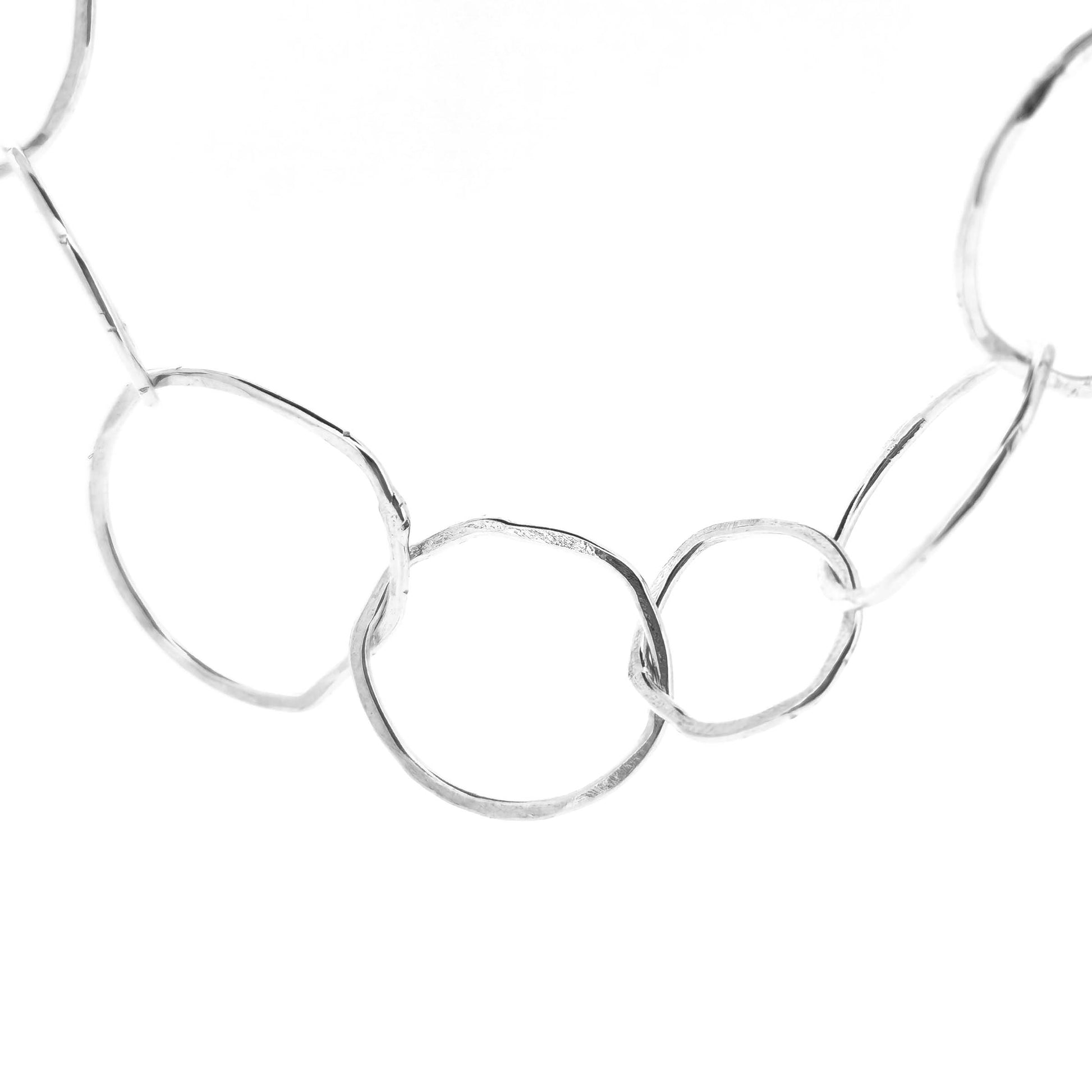 Part of a silver necklace with rustic interlocking circular links on a white back ground