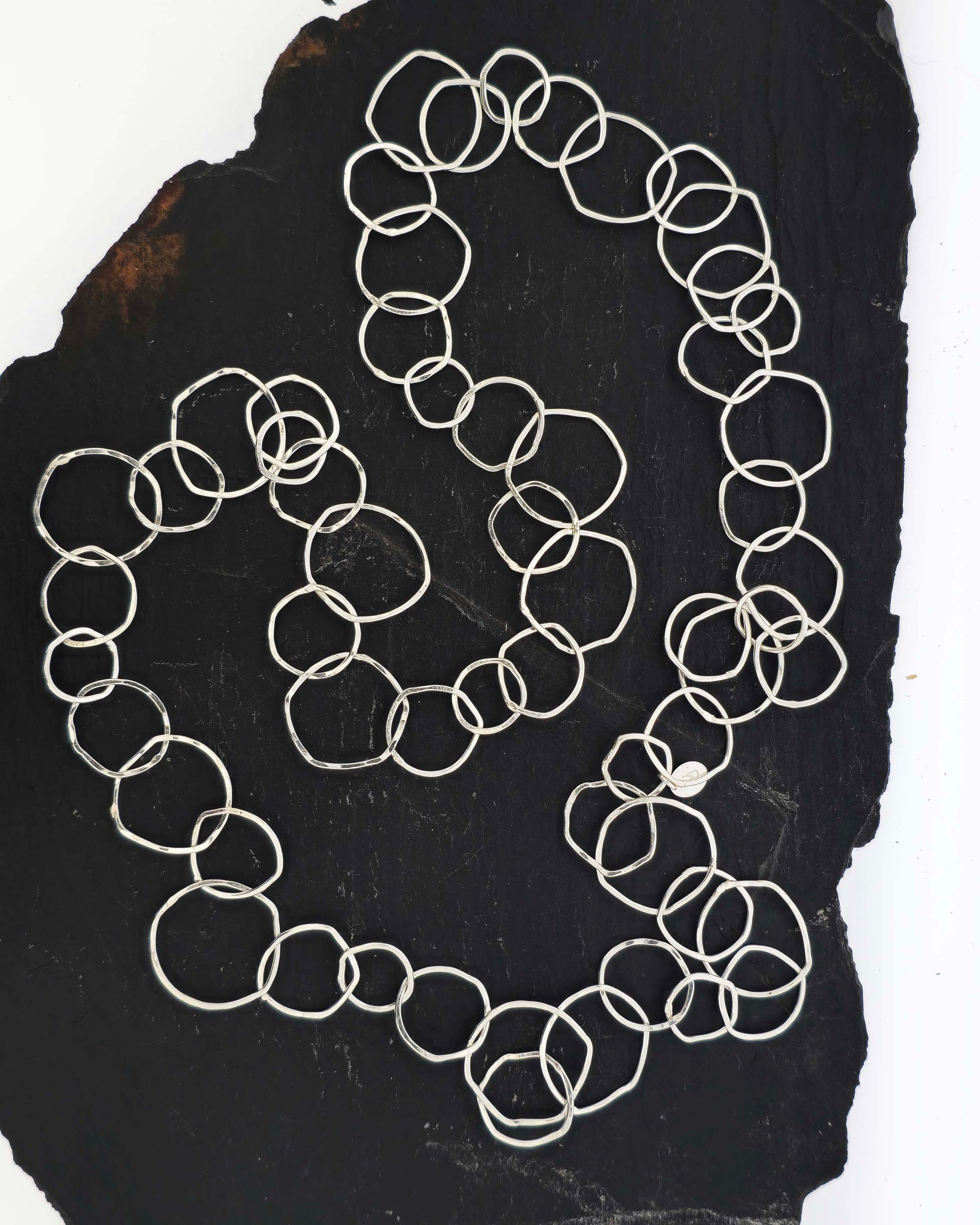 Silver necklace with rustic interlocking circular links on a slate back ground