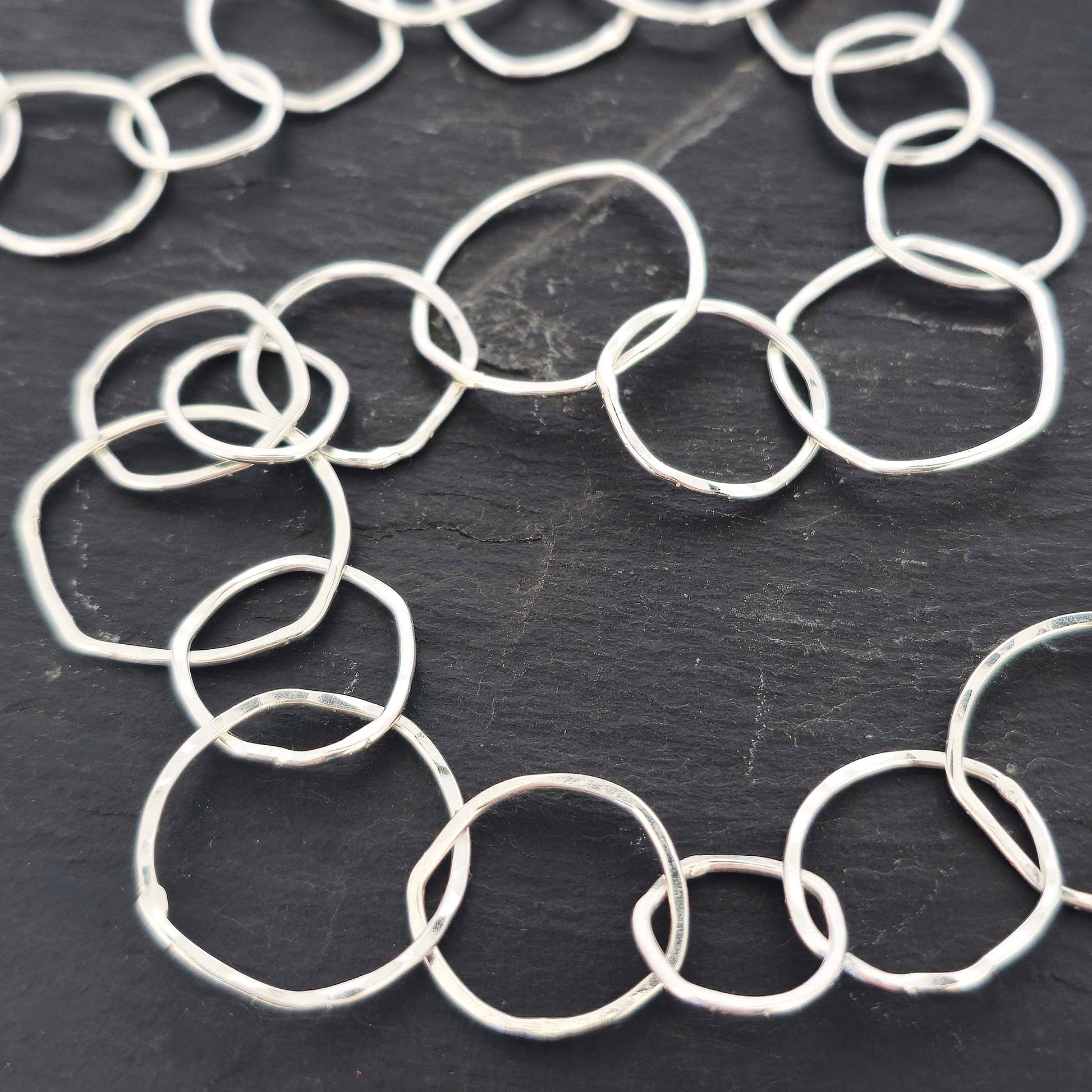 Silver necklace with rustic interlocking circular links on a slate back ground