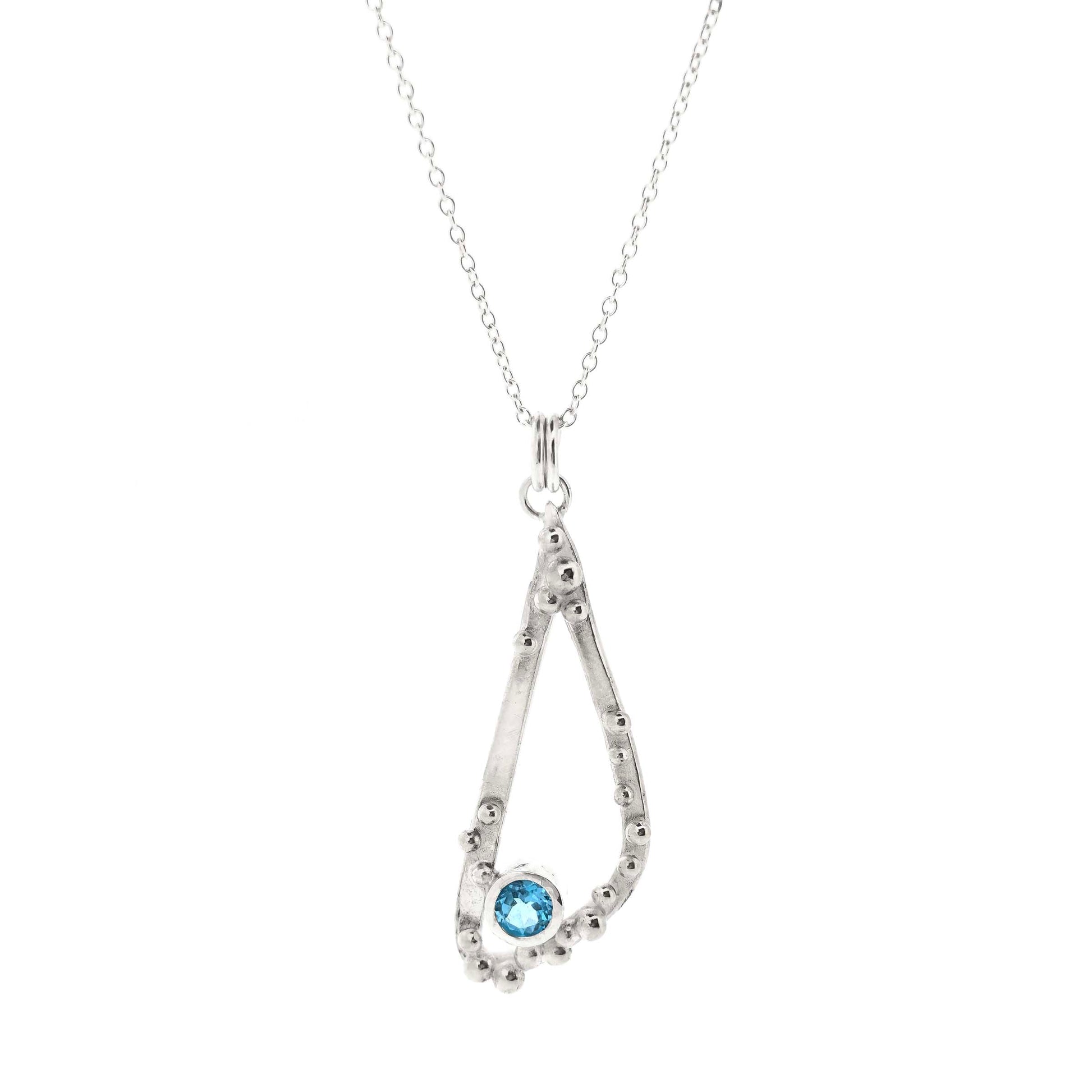 Silver asymmetrical soft open triangle pendant with silver balls and a blue topaz gemstone on a silver chain. Shown on a white background.