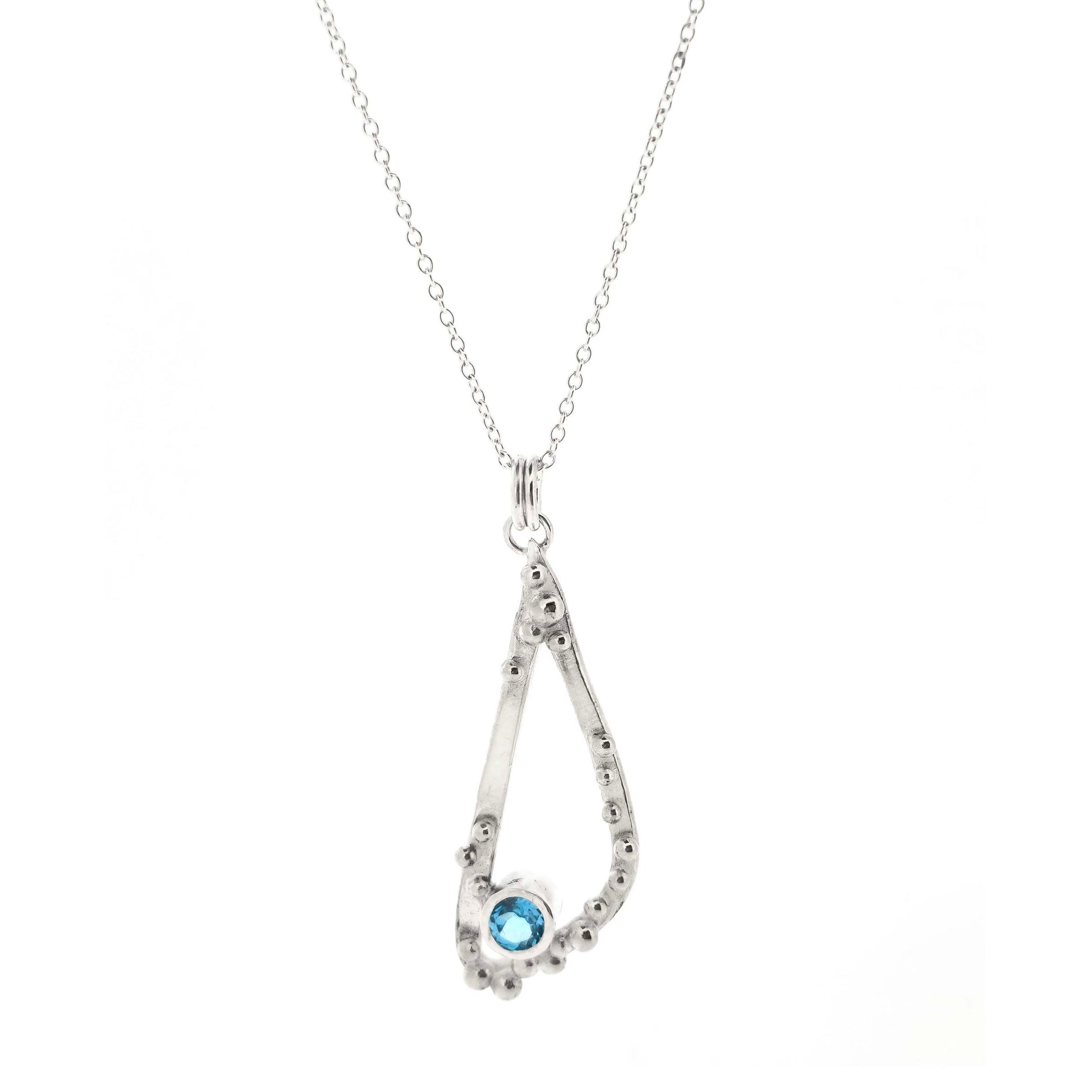 Silver asymmetrical soft open triangle pendant with silver balls and a blue topaz gemstone on a silver chain. Shown on a white bcakground.