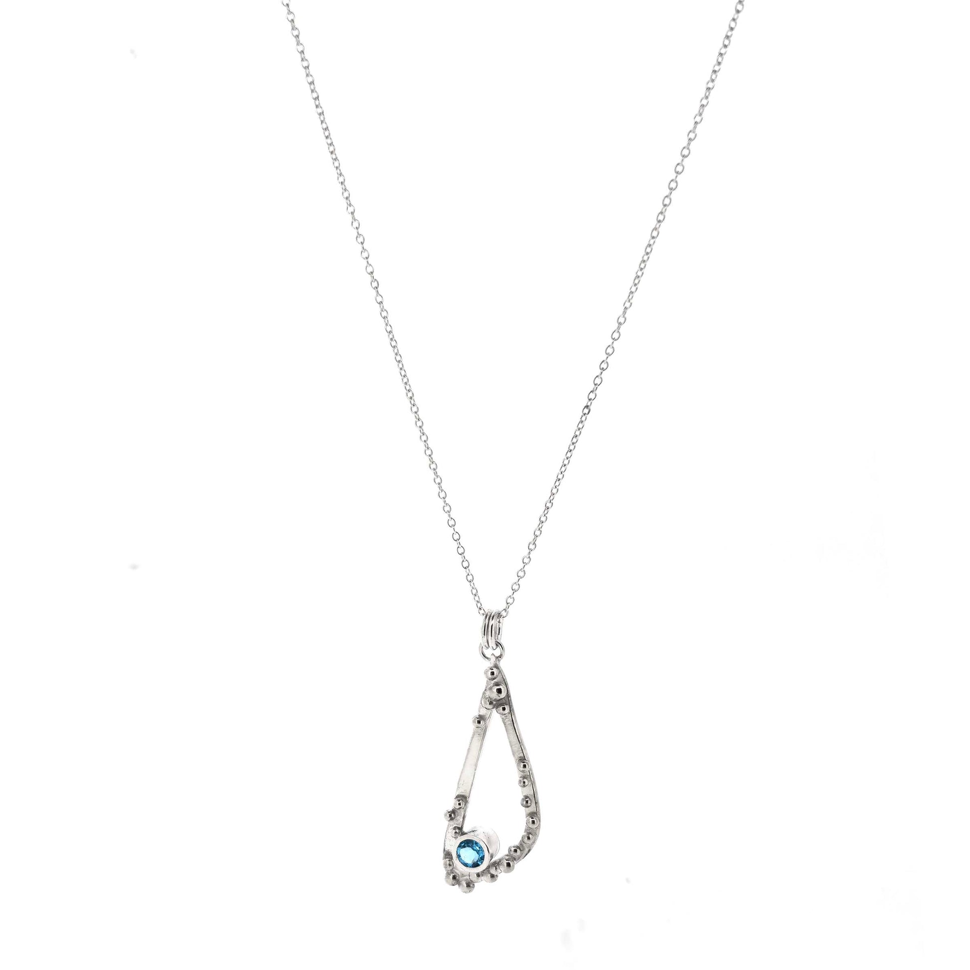 Silver asymmetrical soft open triangle pendant with silver balls and a blue topaz gemstone on a silver chain. Shown on a white background.