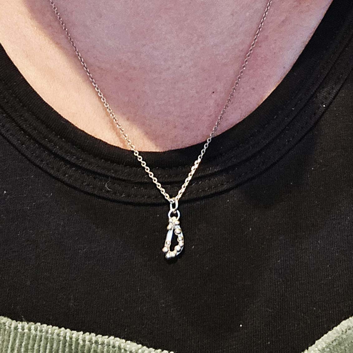 Silver asymmetric open triangle pendant with silver balls on a silver chain. Shown on a person.