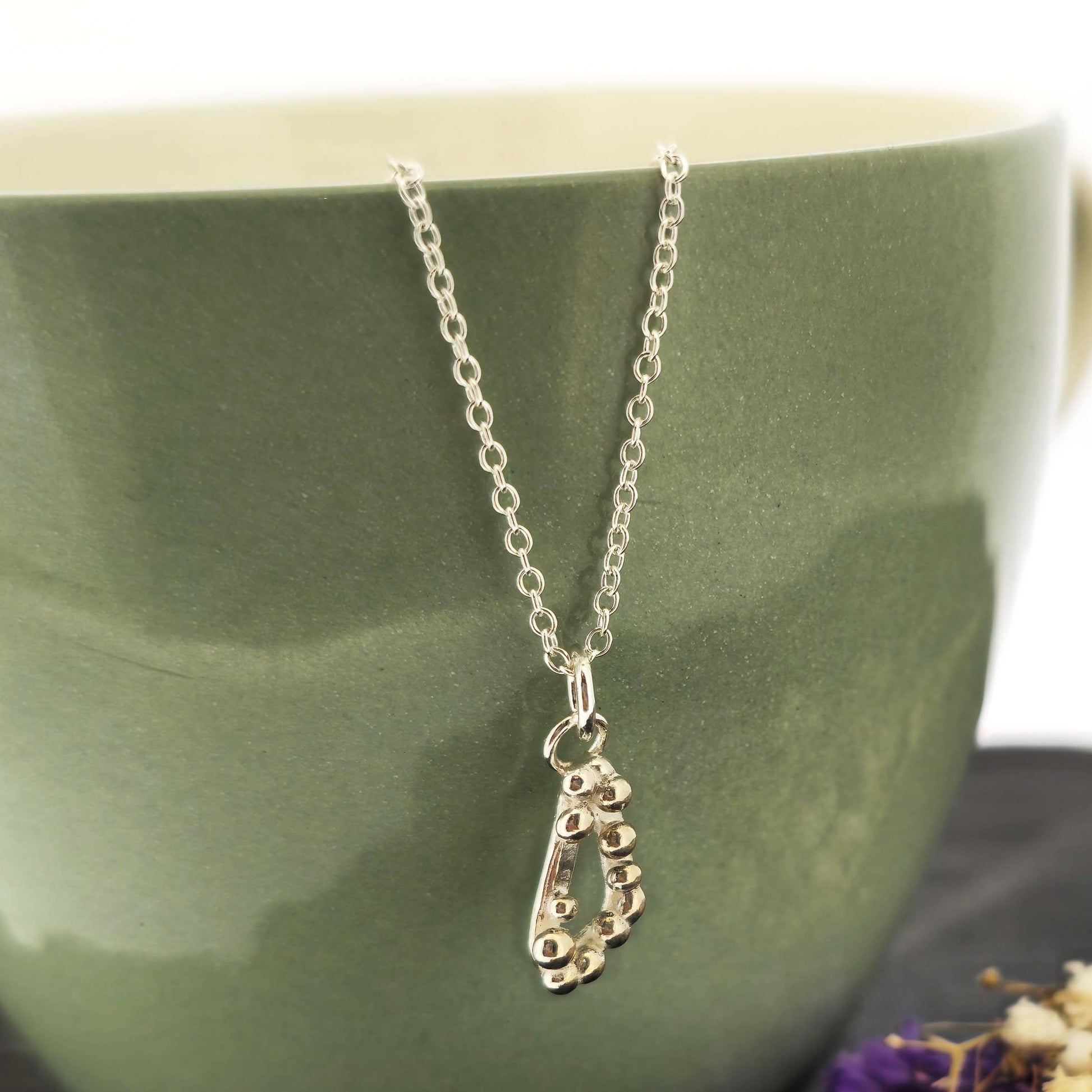 Silver asymmetric open triangle pendant with silver balls on a silver chain. Shown on a green bowl with flowers.