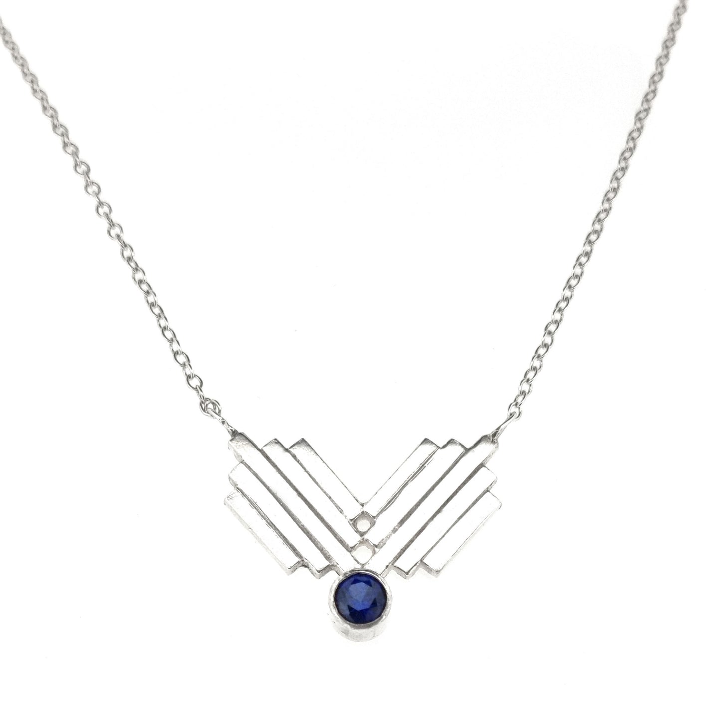 A silver Art Deco style necklace with a focal point of 2 lined elements and a dark blue sapphire gemstone.