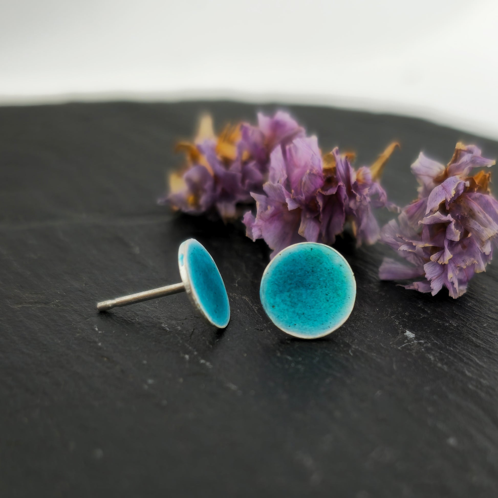 Silver round stud earrings with turquoise enamel. Pictured on slate with flowers.