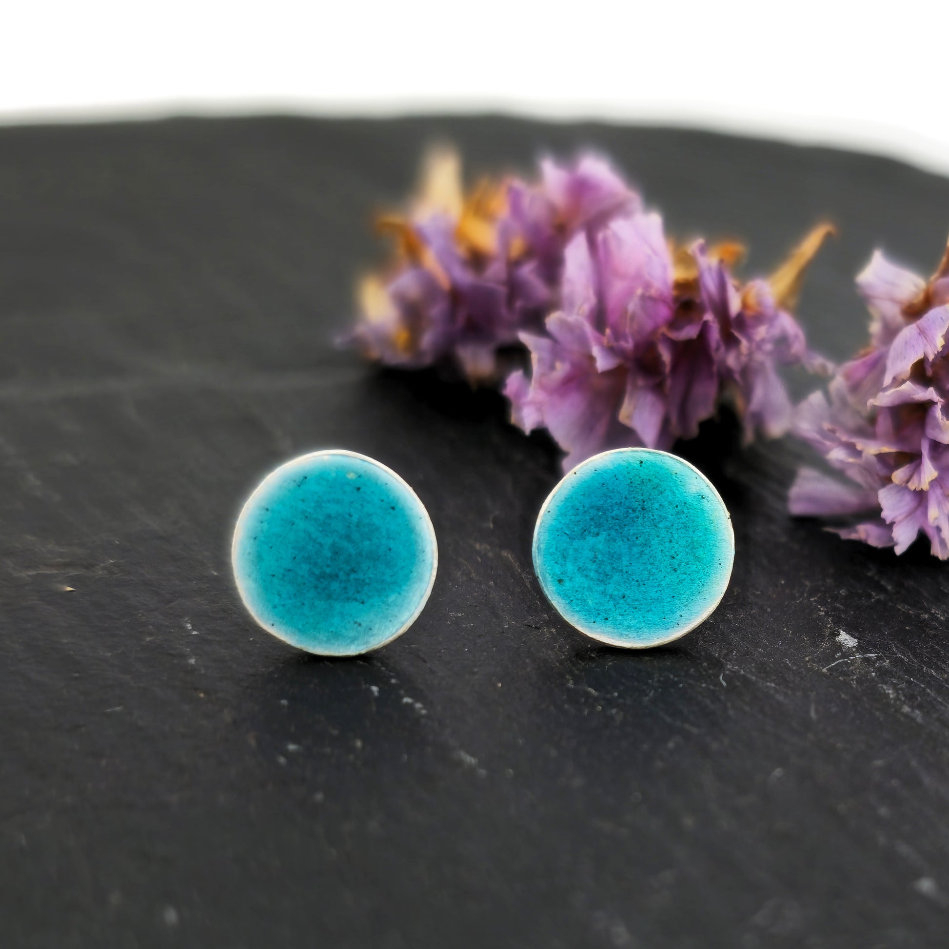 Silver round stud earrings with turquoise enamel. Pictured on slate with flowers.