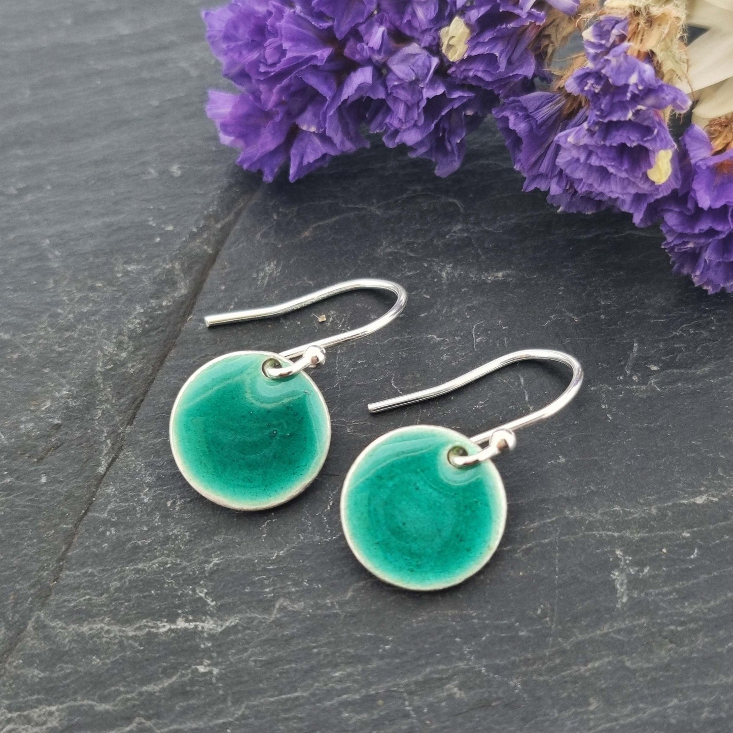 Silver drop earrings with a round disc covered in turquoise green enamel.