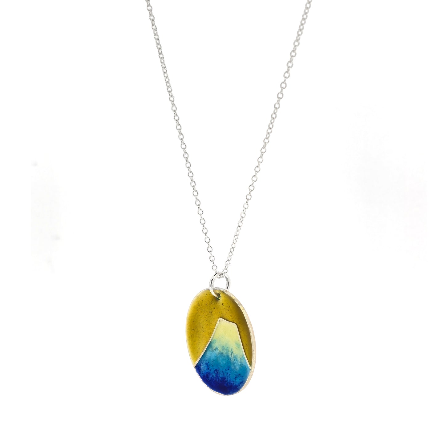 Round silver pendant with a mountain on in graduated blue enamel and a white top and a yellow enamel background. Suspended from a silver chain. Side view.