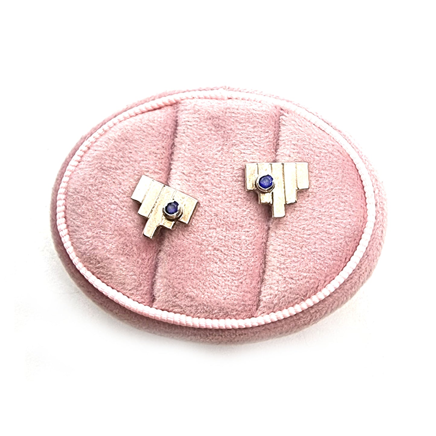 Silver Art Deco style stud earrings with 5 silver lines and off-centre dark blue sapphires. Pictured in a jewellery box.
