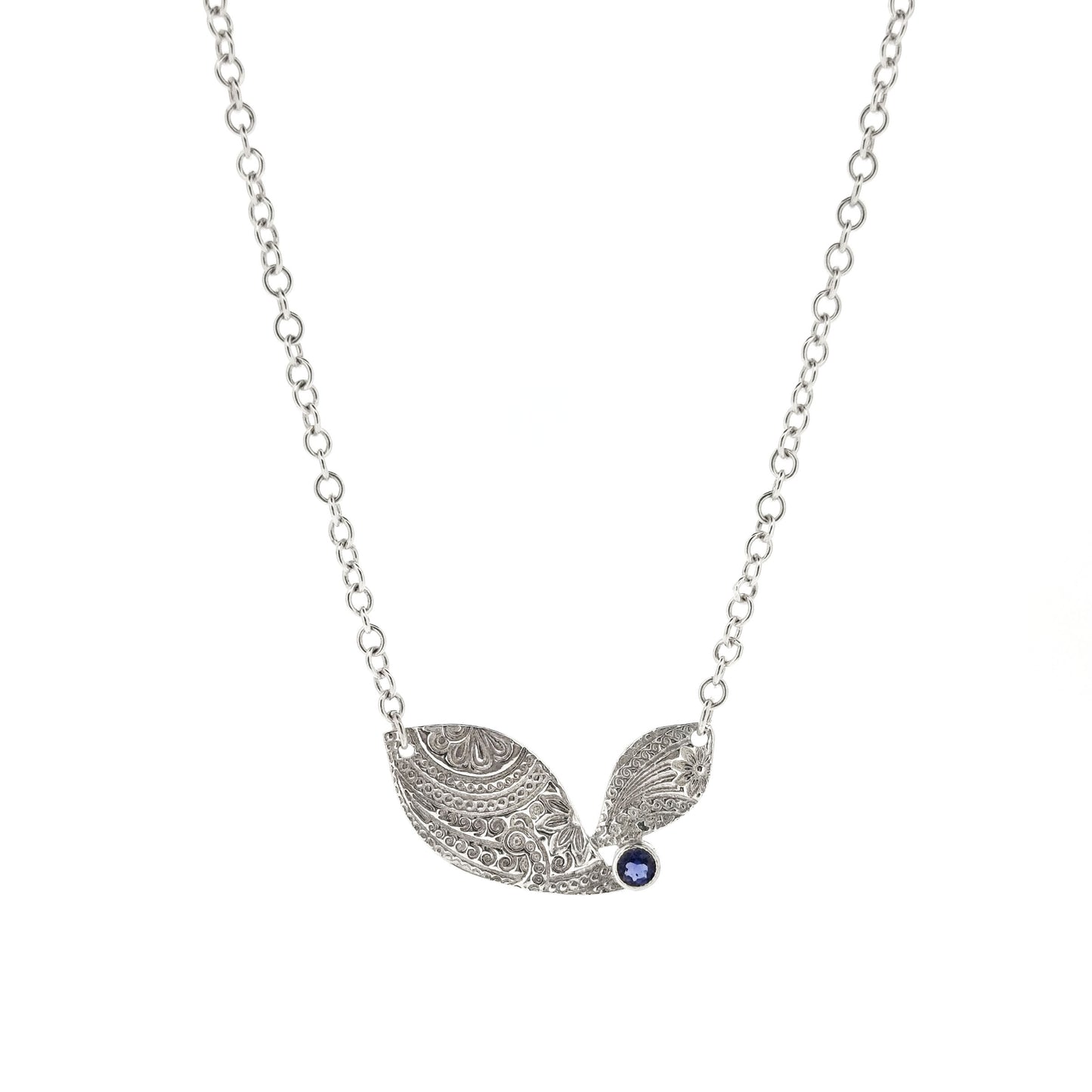 An asymmetric silver necklace with a patterned focal point set with a blue/purple gemstone