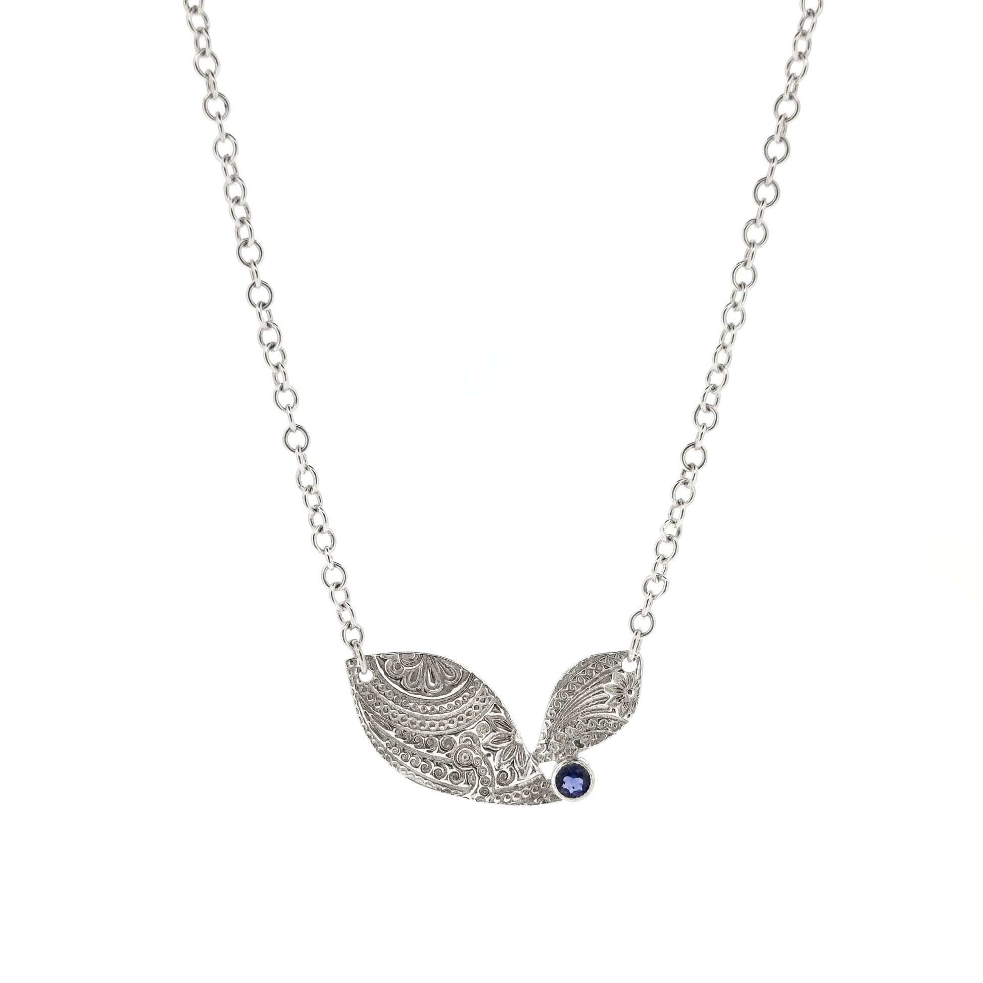 An asymmetric silver necklace with a patterned focal point set with a blue/purple gemstone