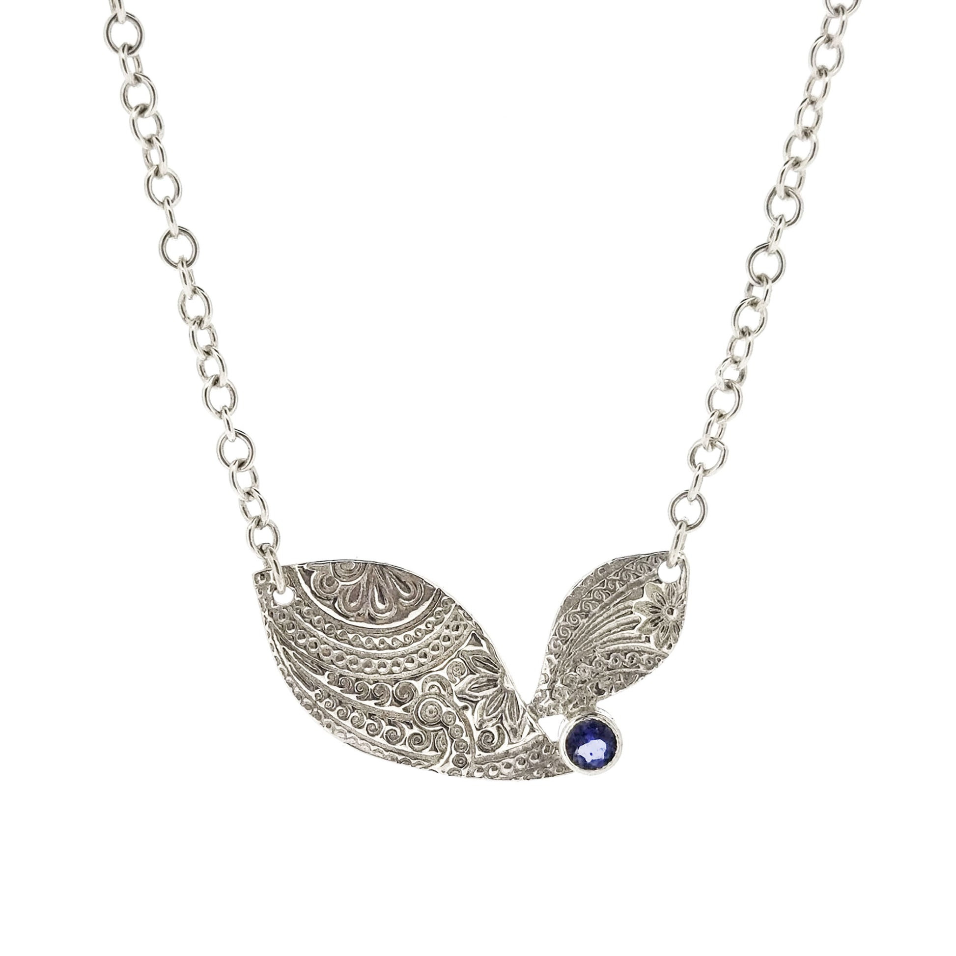 An asymmetric silver necklace with a patterned focal point set with a blue/purple gemstone