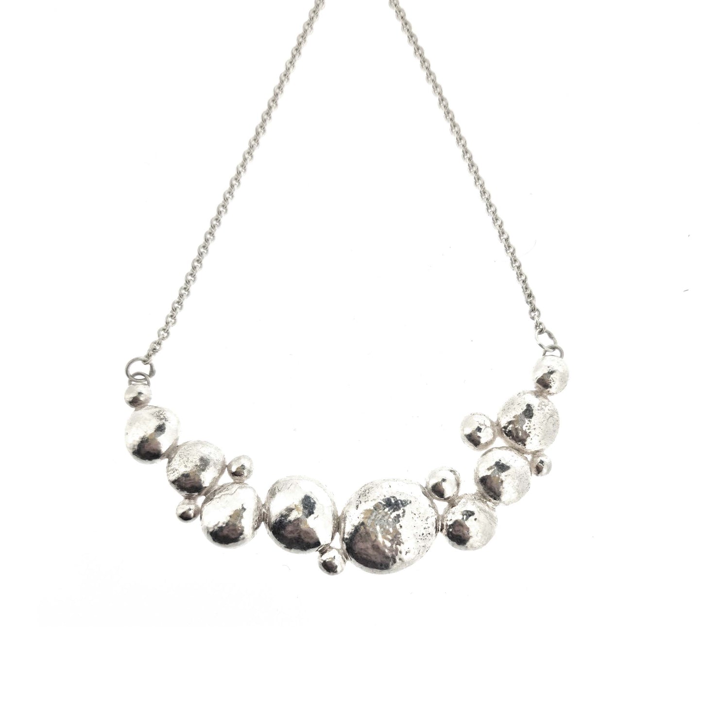 A silver necklace with a curve made up of silver balls of various sizes and with a chain necklace.