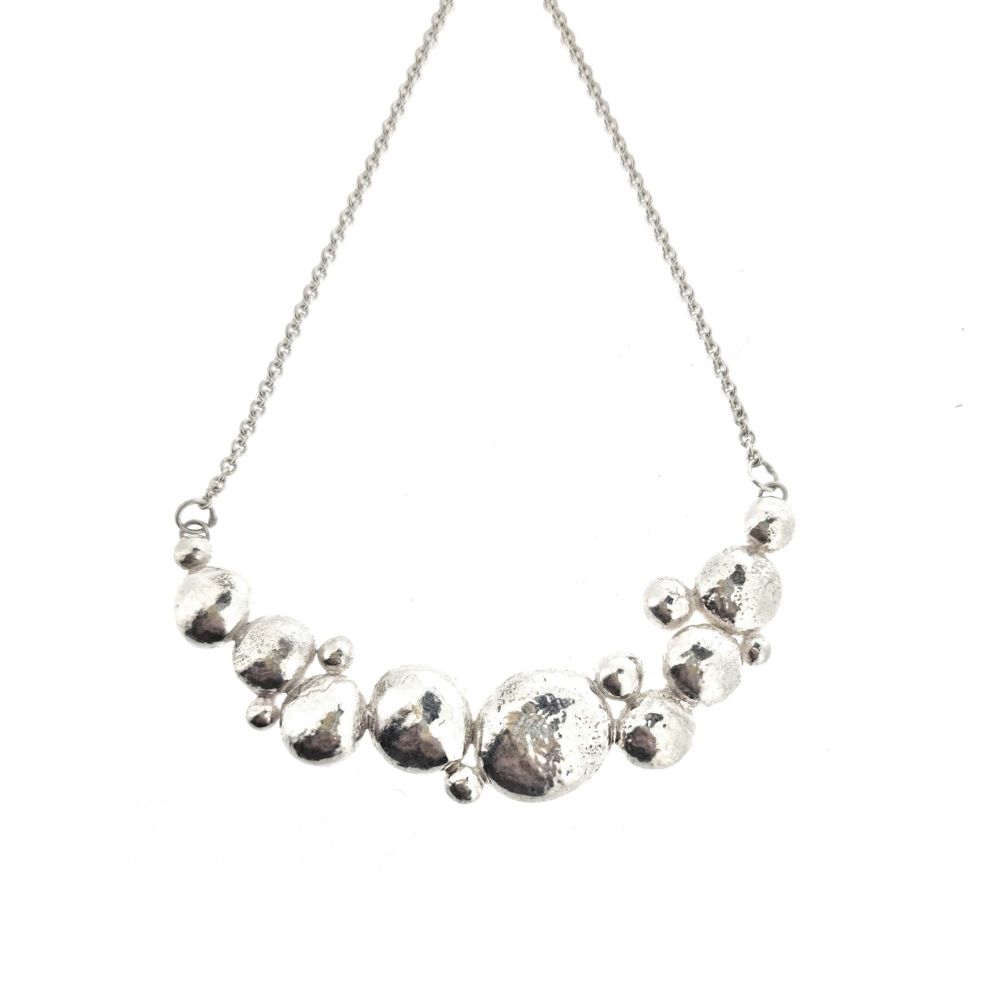 A silver necklace with a curve made up of silver balls of various sizes and with a chain necklace.