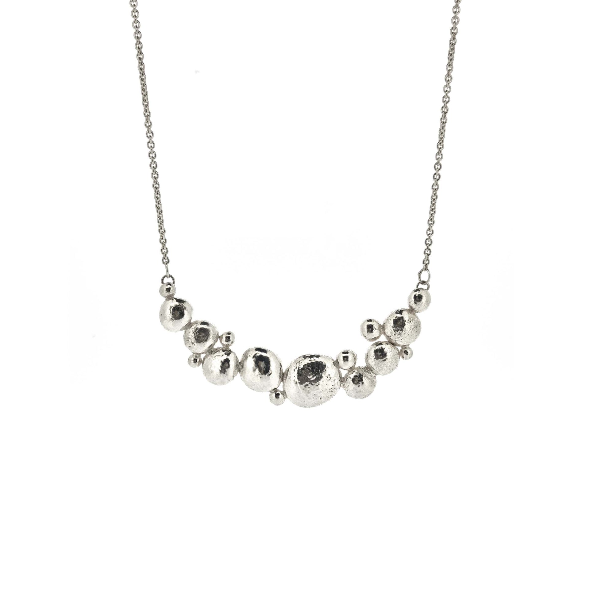 A silver necklace with a curve made up of silver balls of various sizes and with a chain necklace.