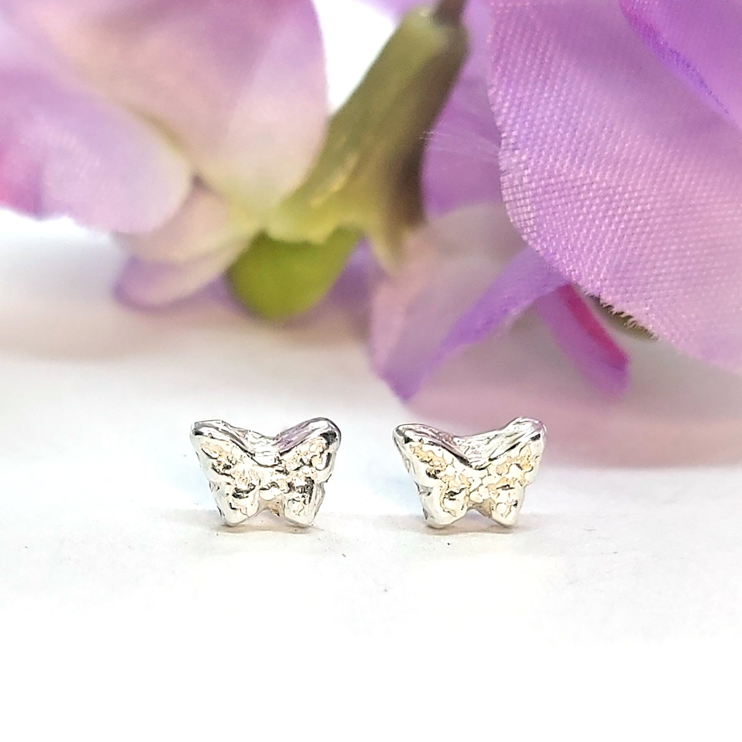 Tiny textured butterfly stud earrings. Pictured with flowers.