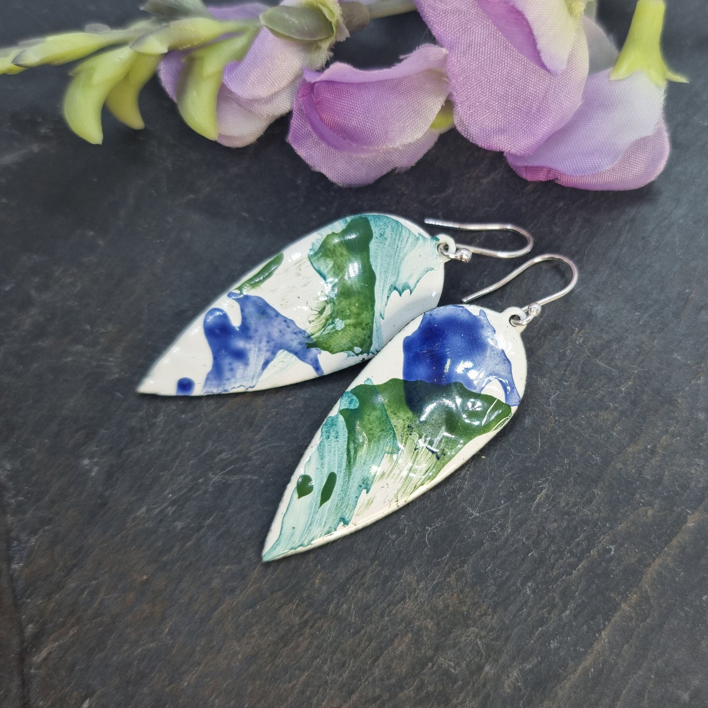 Large teardrop-shaped enamel drop earrings with splashes of dark blue and green on a white background - with flowers