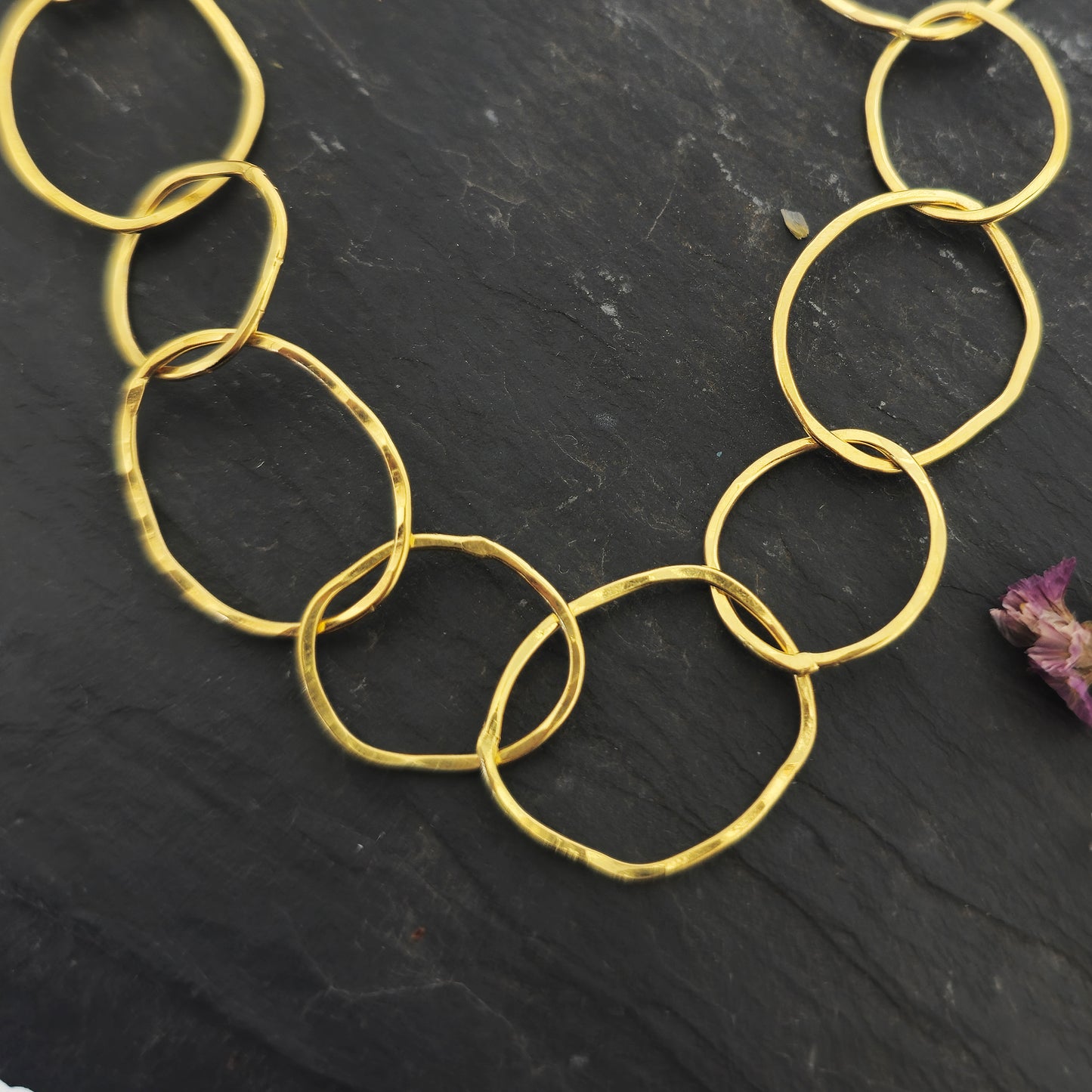 A yellow gold vermeil chain necklace with organic style circular links. Pictured on slate with flowers.