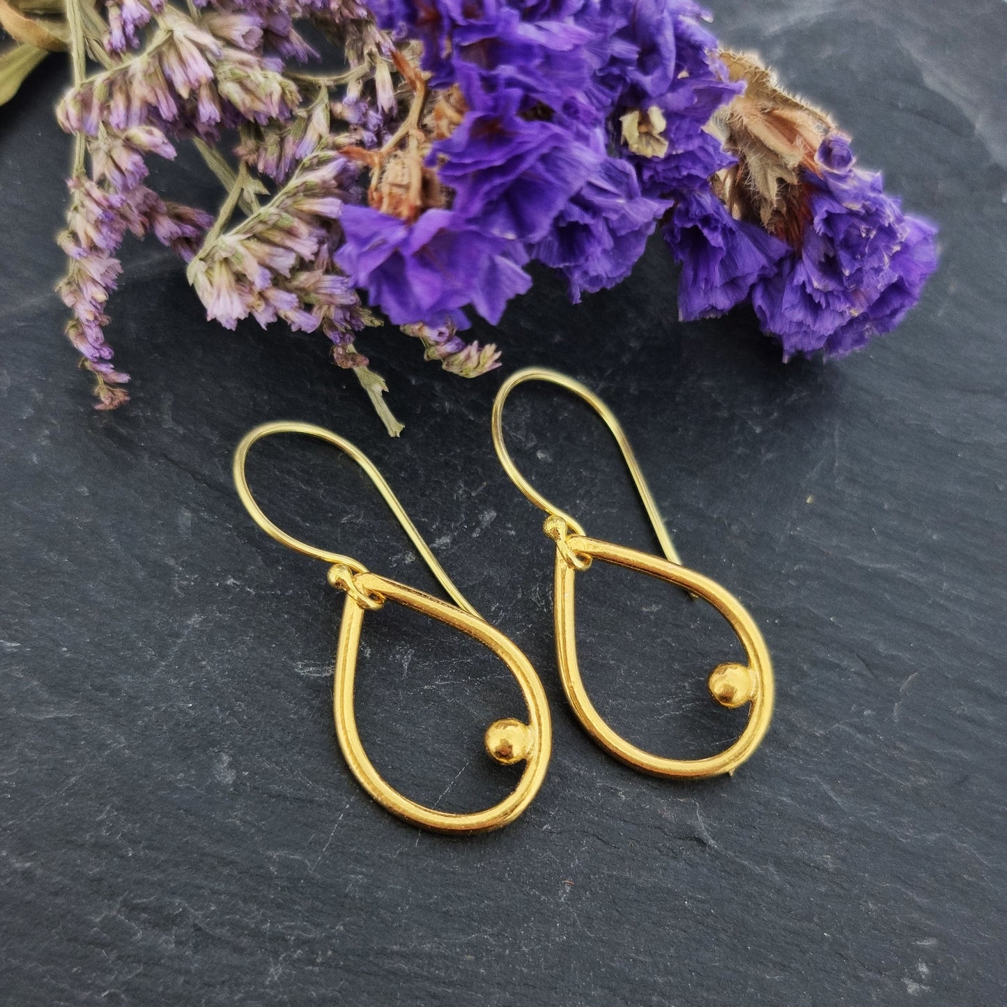 Yellow gold vermeil open teardrop with off-center ball drop earrings. Pictured with flowers.