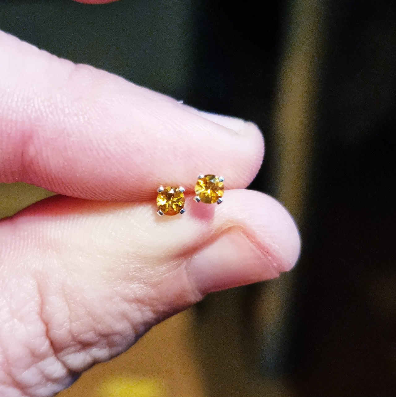 Silver 4 claw stud earrings with golden yellow citrine gemstones. Shown held between 2 fingers.