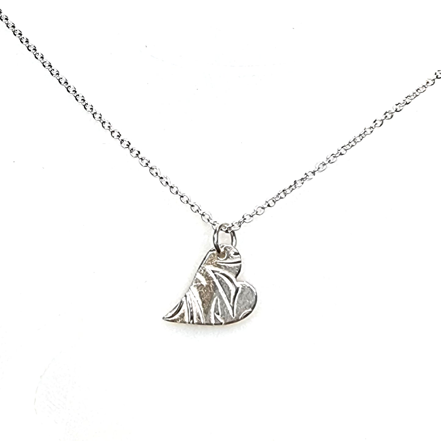 A silver asymmetrical heart pendant with a leaf and vine pattern suspended on a silver chain - small