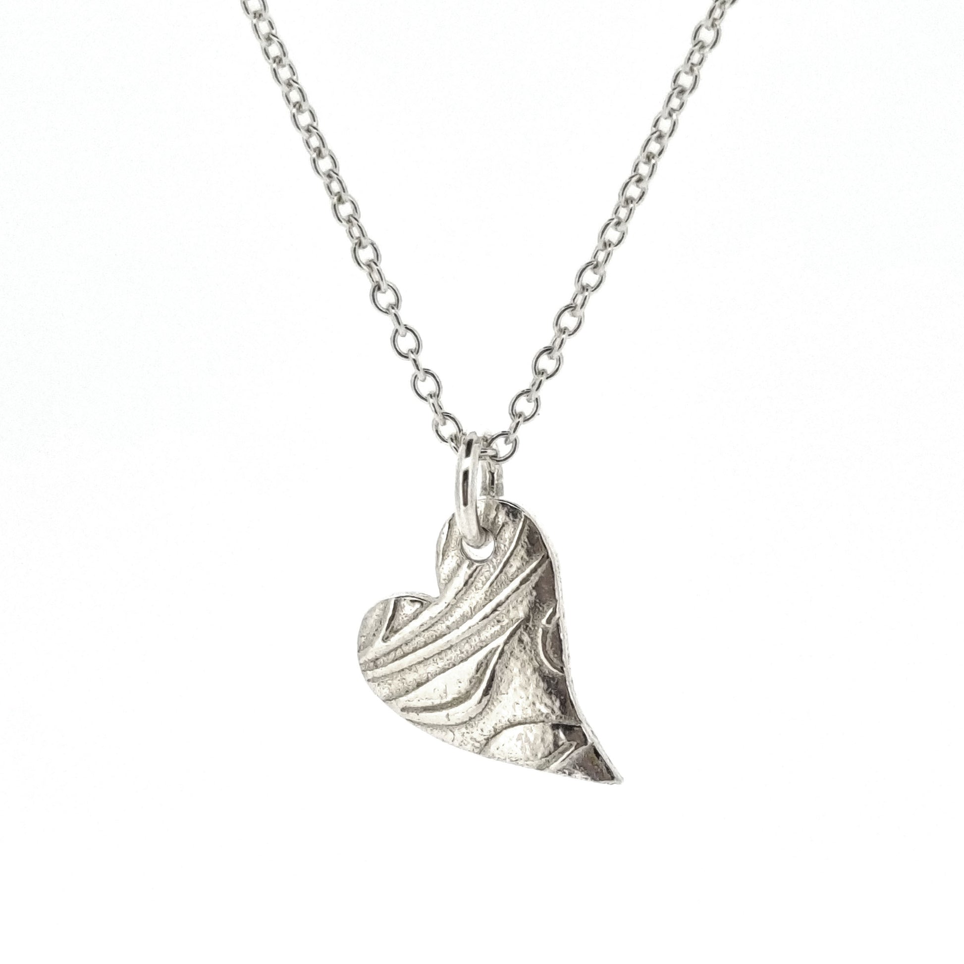 A silver asymmetrical heart pendant with a leaf and vine pattern suspended on a silver chain - small