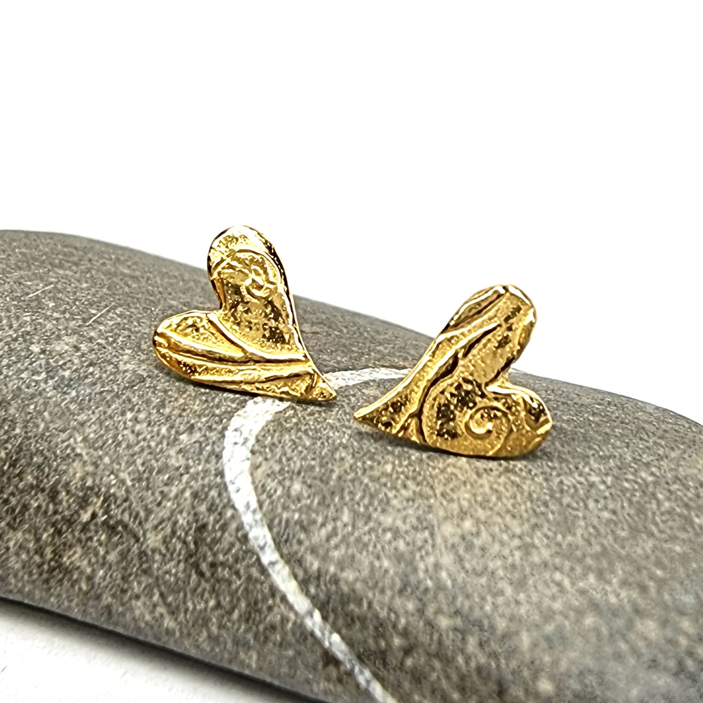 Yellow gold vermeil asymmetrical heart stud earrings with a swirl pattern. Pictured on a pebble.