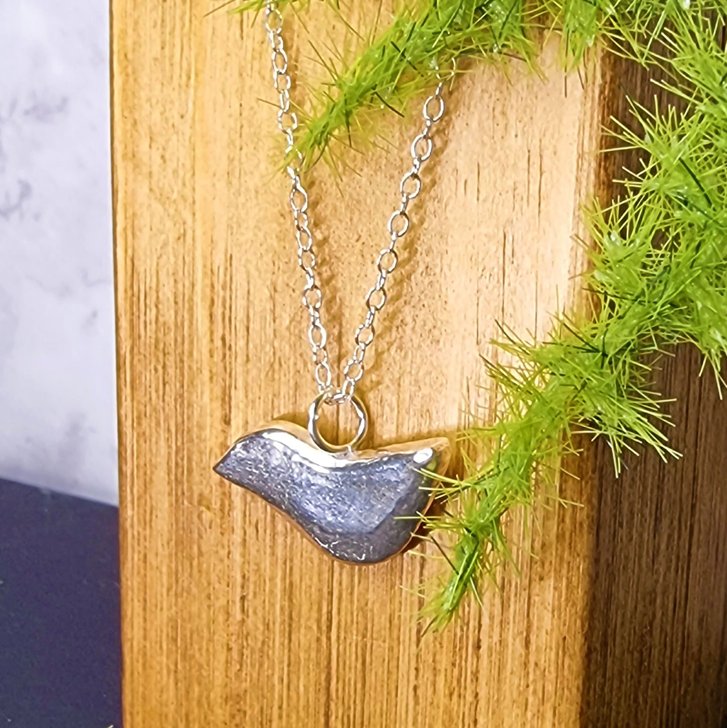 A silver stylised bird pendant on a silver chain.