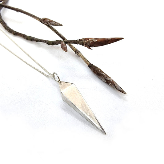 A silver geometric diamond shaped pendant on a silver chain. Pictured with a twig.