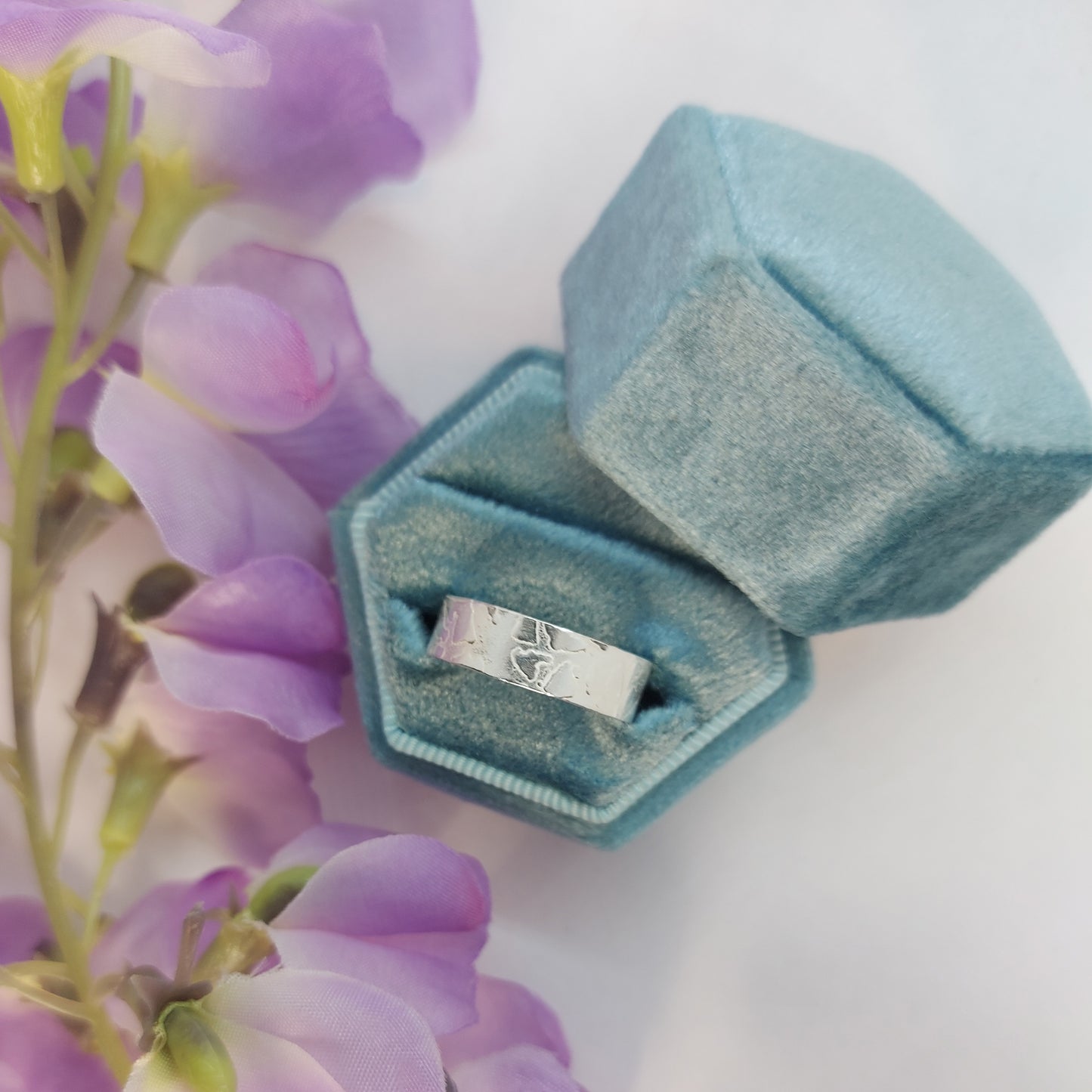 Silver band ring with islands in the sea style pattern. Pictured in a box with flowers.