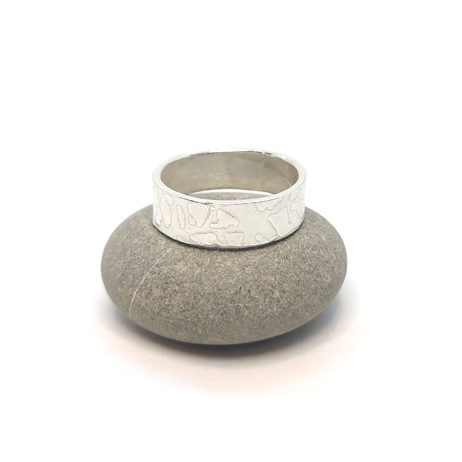 Silver band ring with islands in the sea style pattern. Pictured on a pebble.