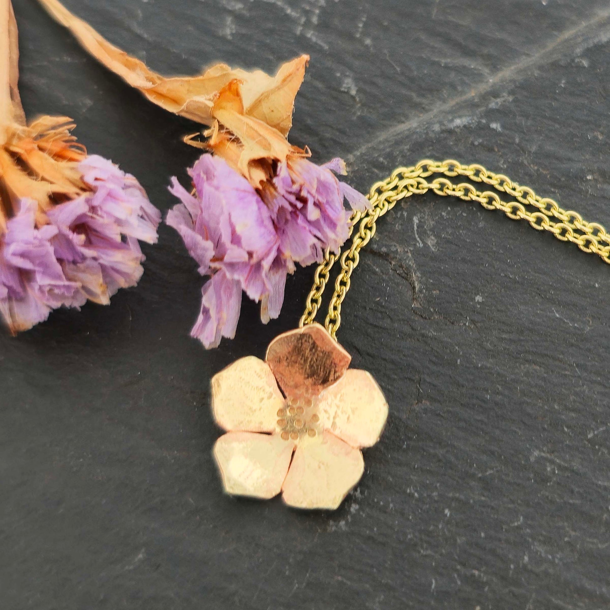 9ct yellow gold flower-shaped pendant necklace on a dark surface with dried flowers.