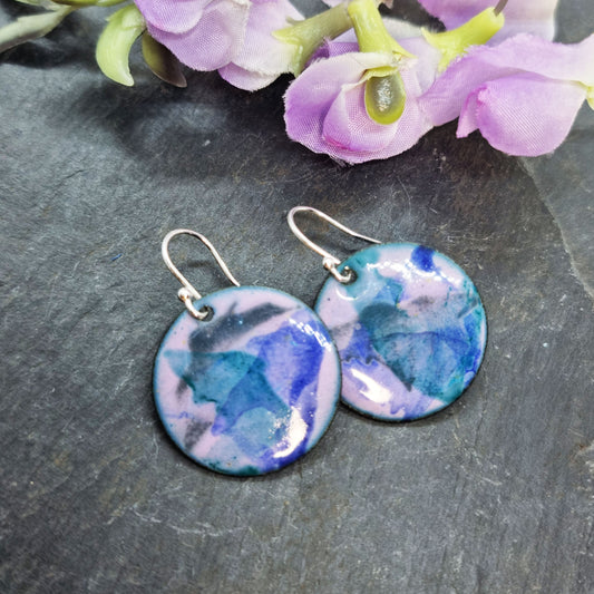 Round enamel drop earrings with splashes of dark blue, green and grey on a light purple background - with flowers