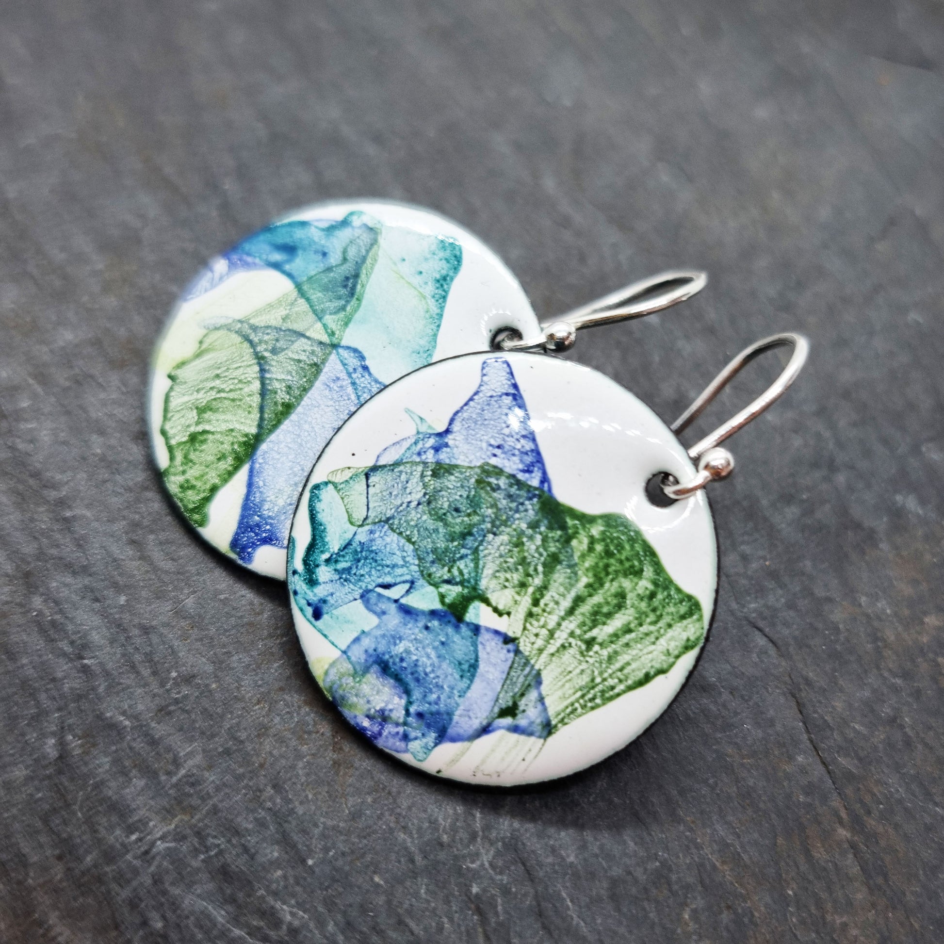 Round enamel drop earrings with splashes of dark blue and green on a white background.