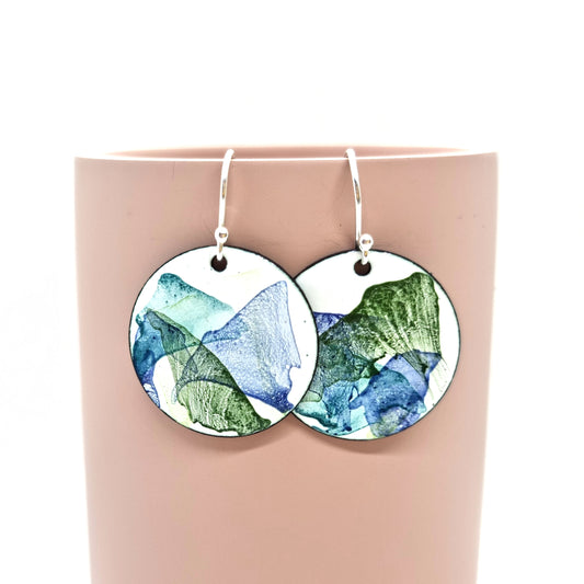 Round enamel drop earrings with splashes of dark blue and green on a white background.