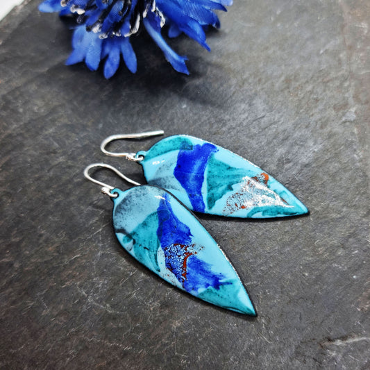 Large teardrop shaped enamel drop earrings with splashes of dark blue, red, green and grey on a light blue background - with flowers